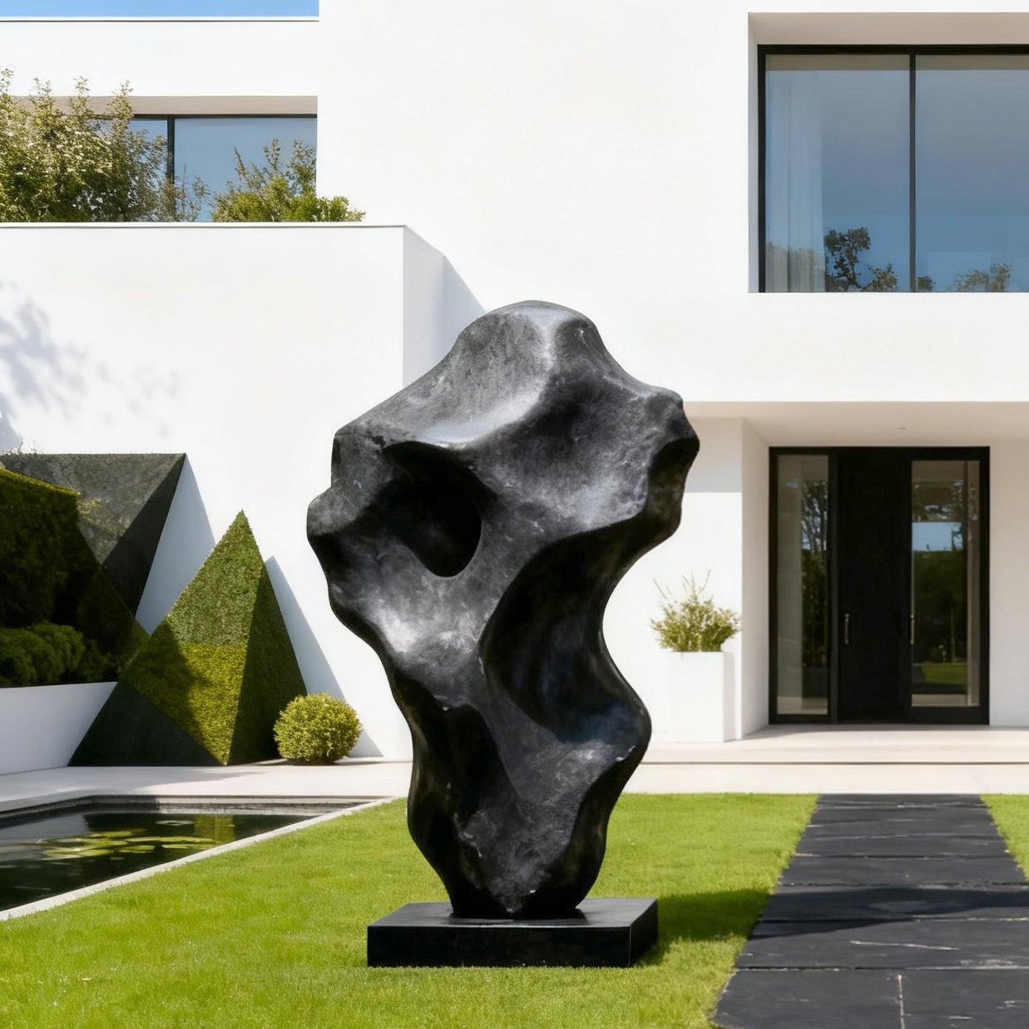 Modern black bronze sculpture in a garden setting with a contemporary house in the background