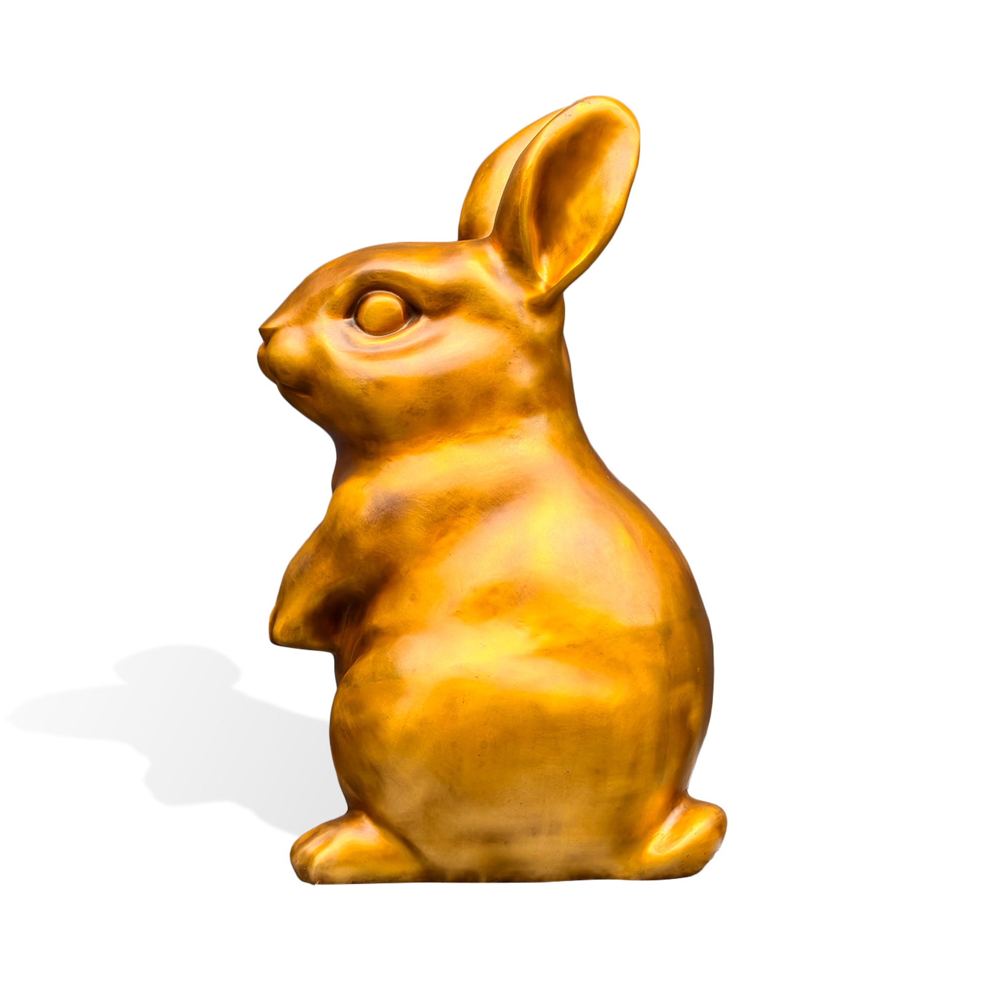 Left-facing side profile of a golden bronze rabbit sculpture with upright ears, a rounded body, sculpted facial features, and a seated pose on a white background.