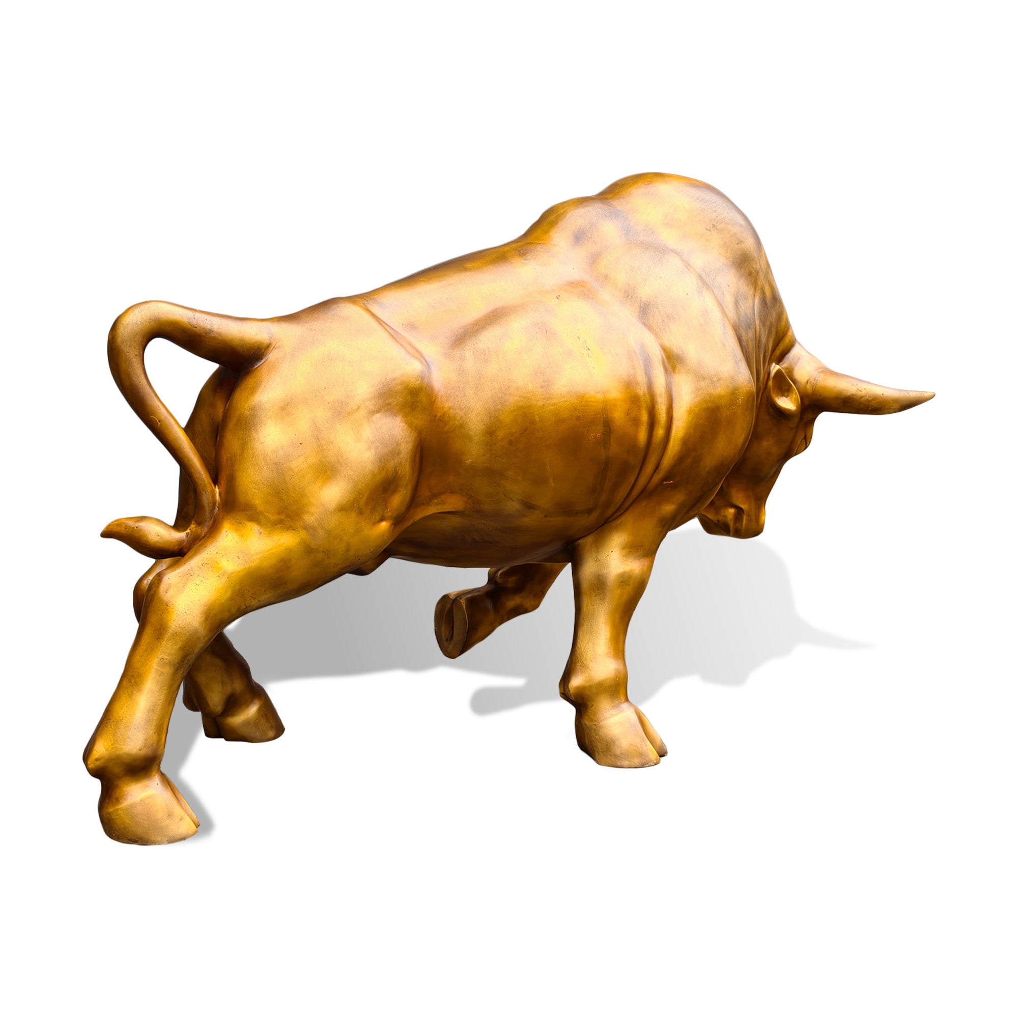 Rear three-quarter view of a golden bronze charging bull sculpture with a lowered head, prominent horns, powerful shoulders, lifted front hoof, and dynamic forward movement