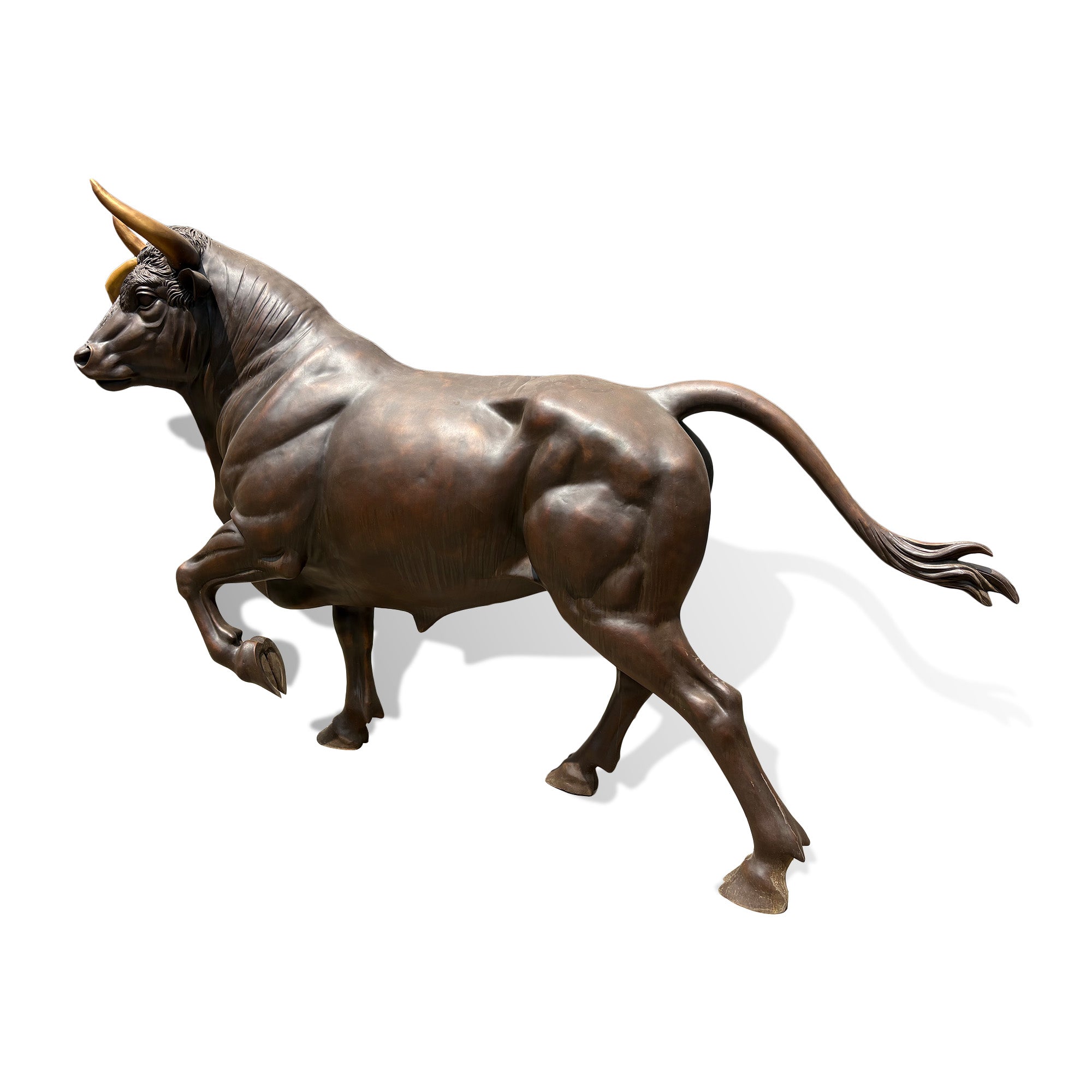Bronze charging bull statue side view showing muscular form, curved horns, detailed body texture, and handcrafted outdoor sculpture design