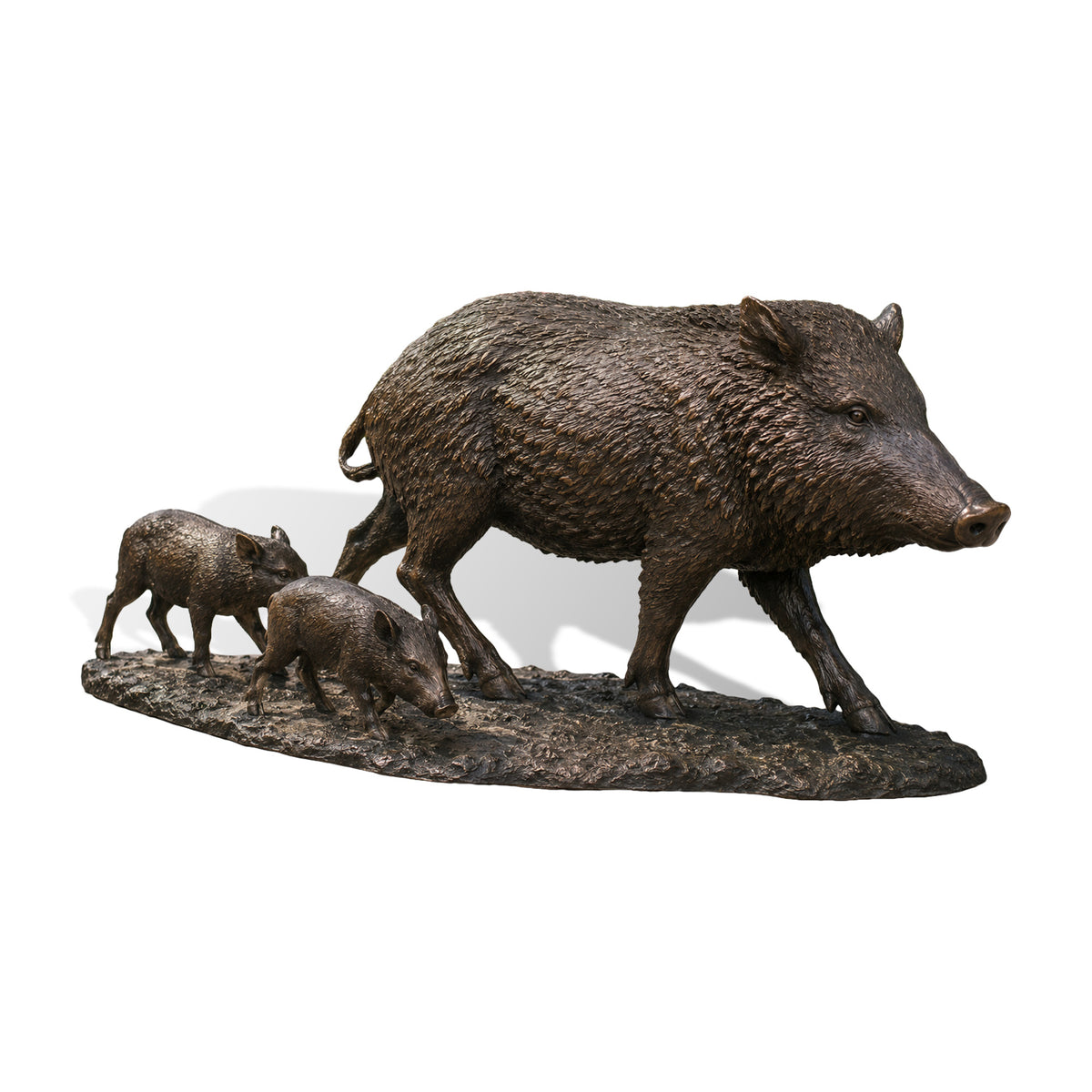 Front view of a bronze wild boar and piglets family sculpture walking on a grassy path, set against a classic red barn and rustic wooden gate on a country farm.