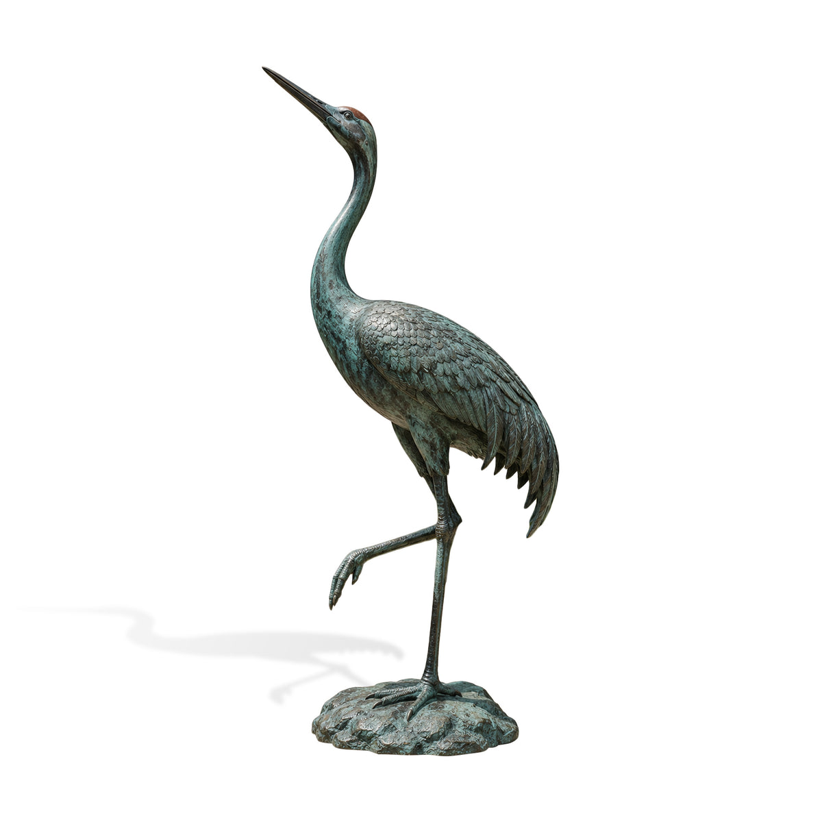 Full-length bronze crane bird sculpture on a textured rock base against a white background, showing a graceful one-legged pose, long upward-curving neck, pointed beak, individually modeled feathers, and green verdigris patina.