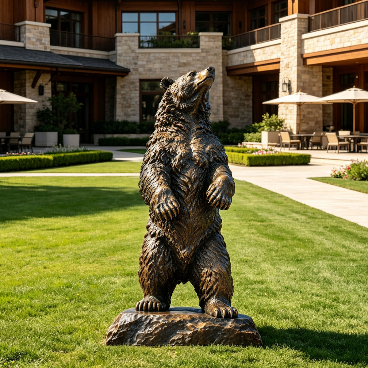 Large standing bronze bear sculpture displayed on a landscaped lawn outside a luxury stone residence, featuring realistic layered fur, raised paws, an upward-looking pose, and a naturalistic rocky base.