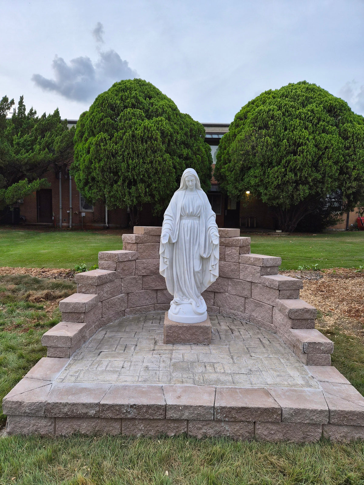 White marble Virgin Mary statue installed outdoors in a Catholic garden prayer area