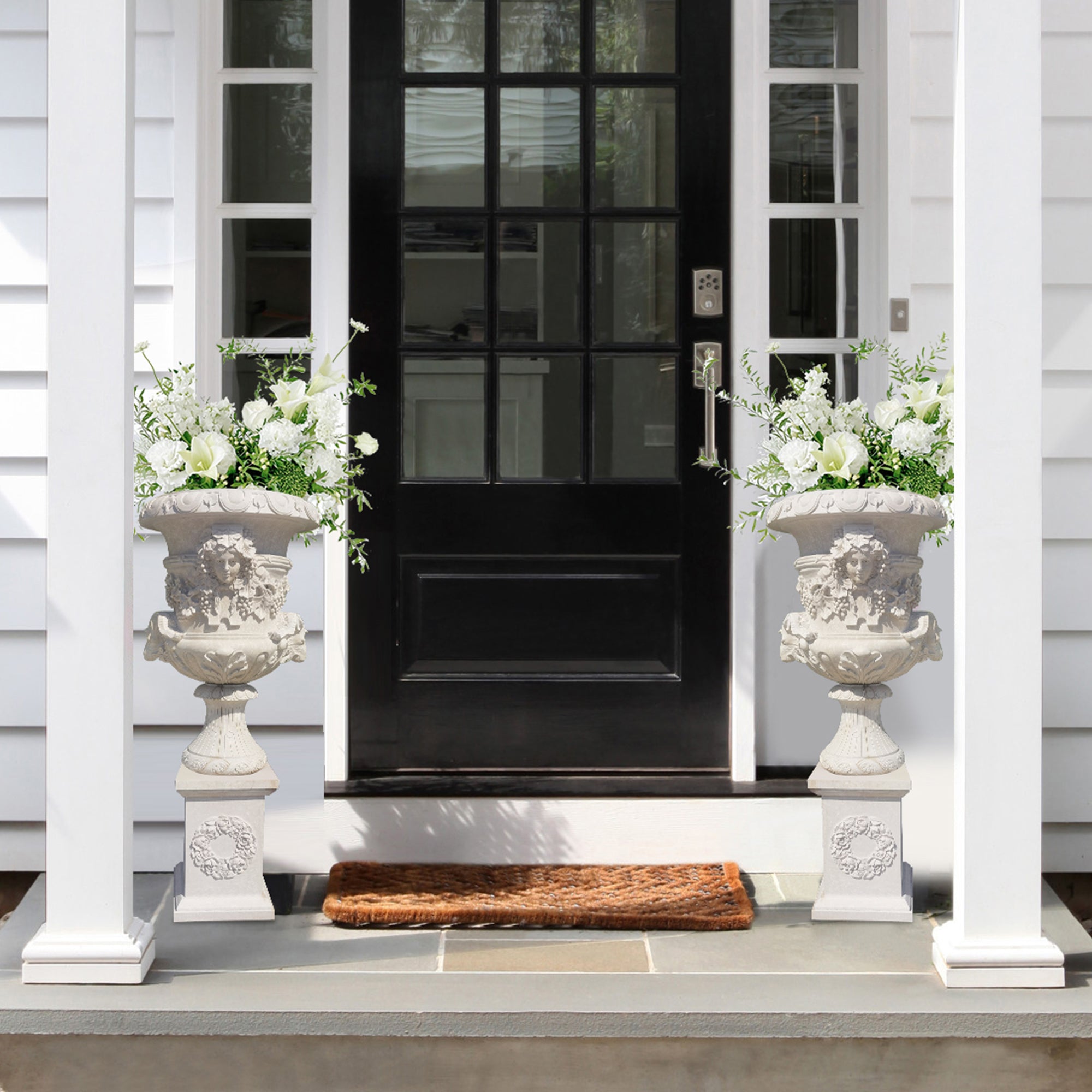 Black front door with decorative urns on either side on a white porch.