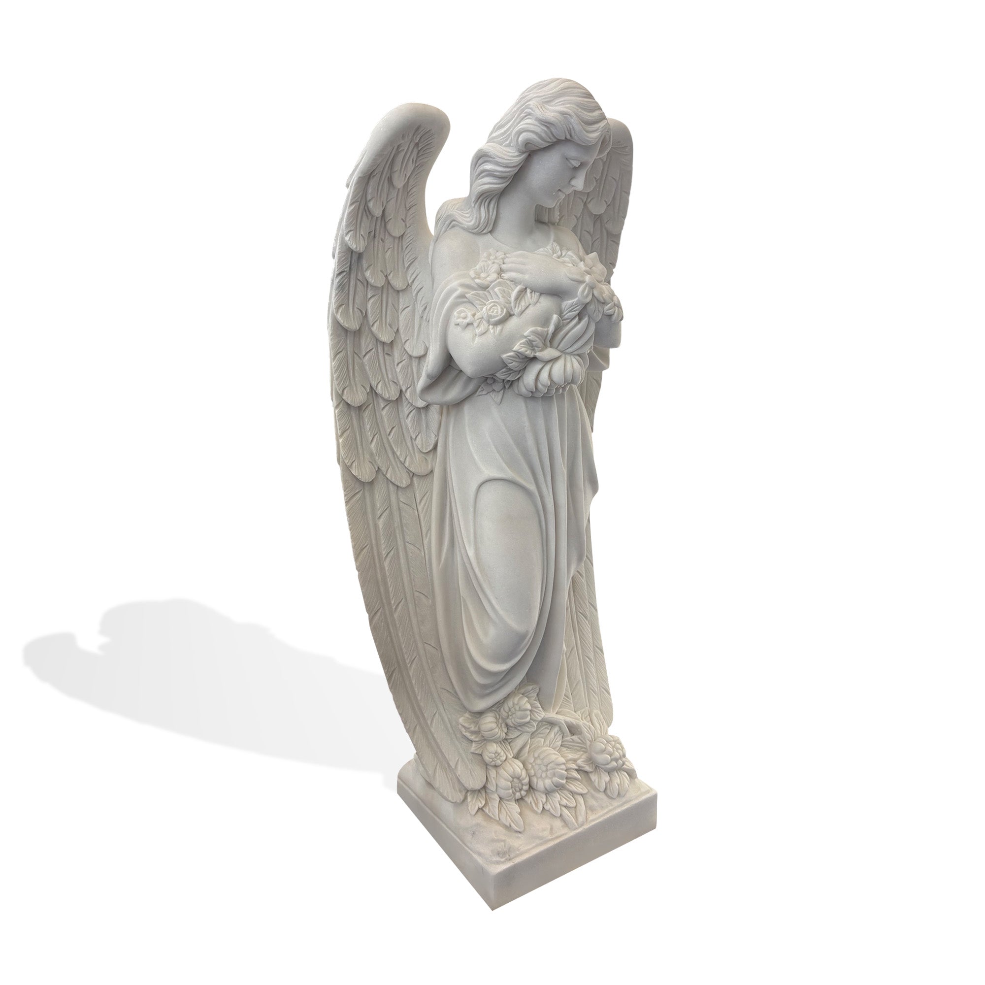 White marble angel statue in side angled view, standing memorial angel sculpture with large wings, bowed head, and flower garland for cemetery or graveyard decor