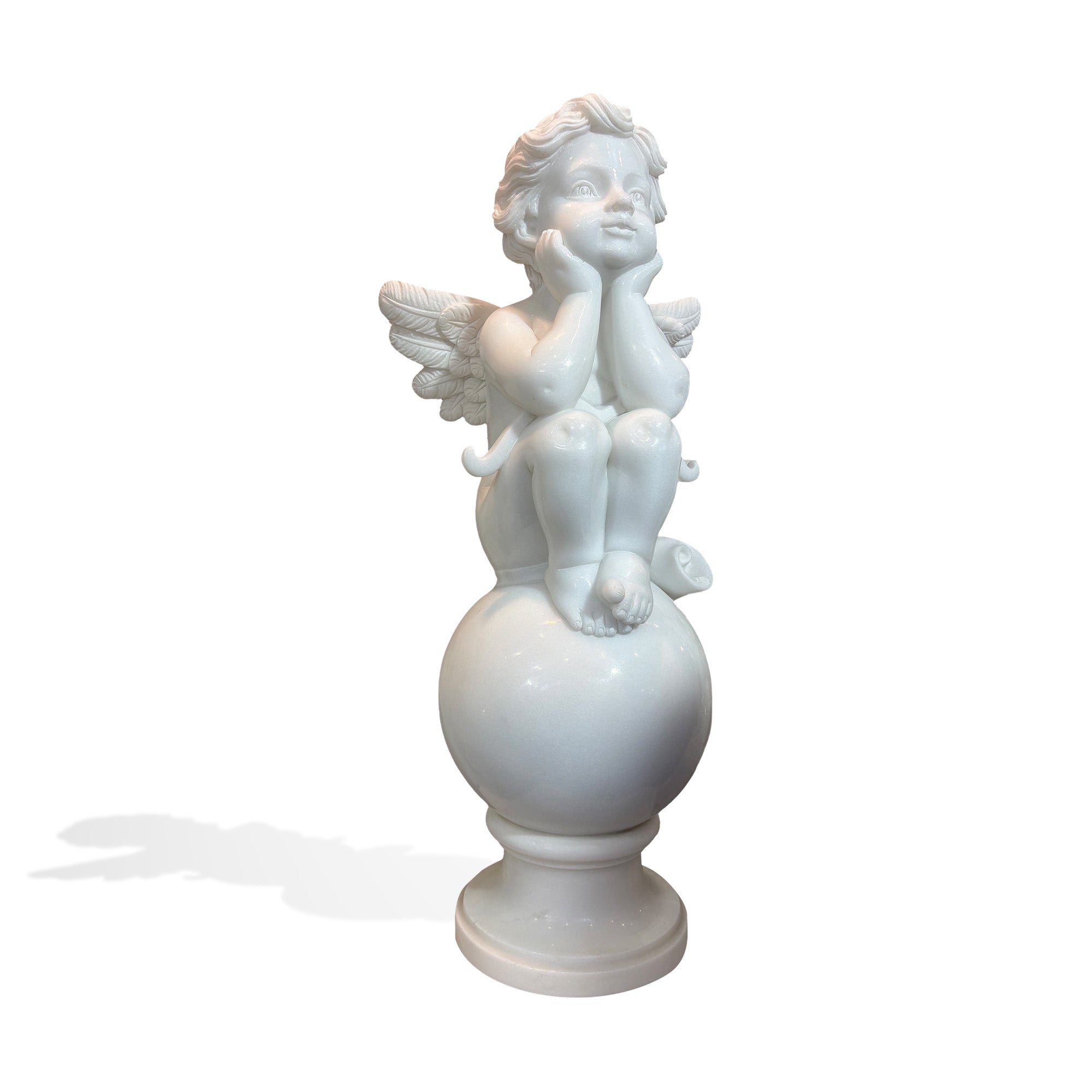 White marble cherub statue seated on a smooth sphere with pedestal base, side view on plain background
