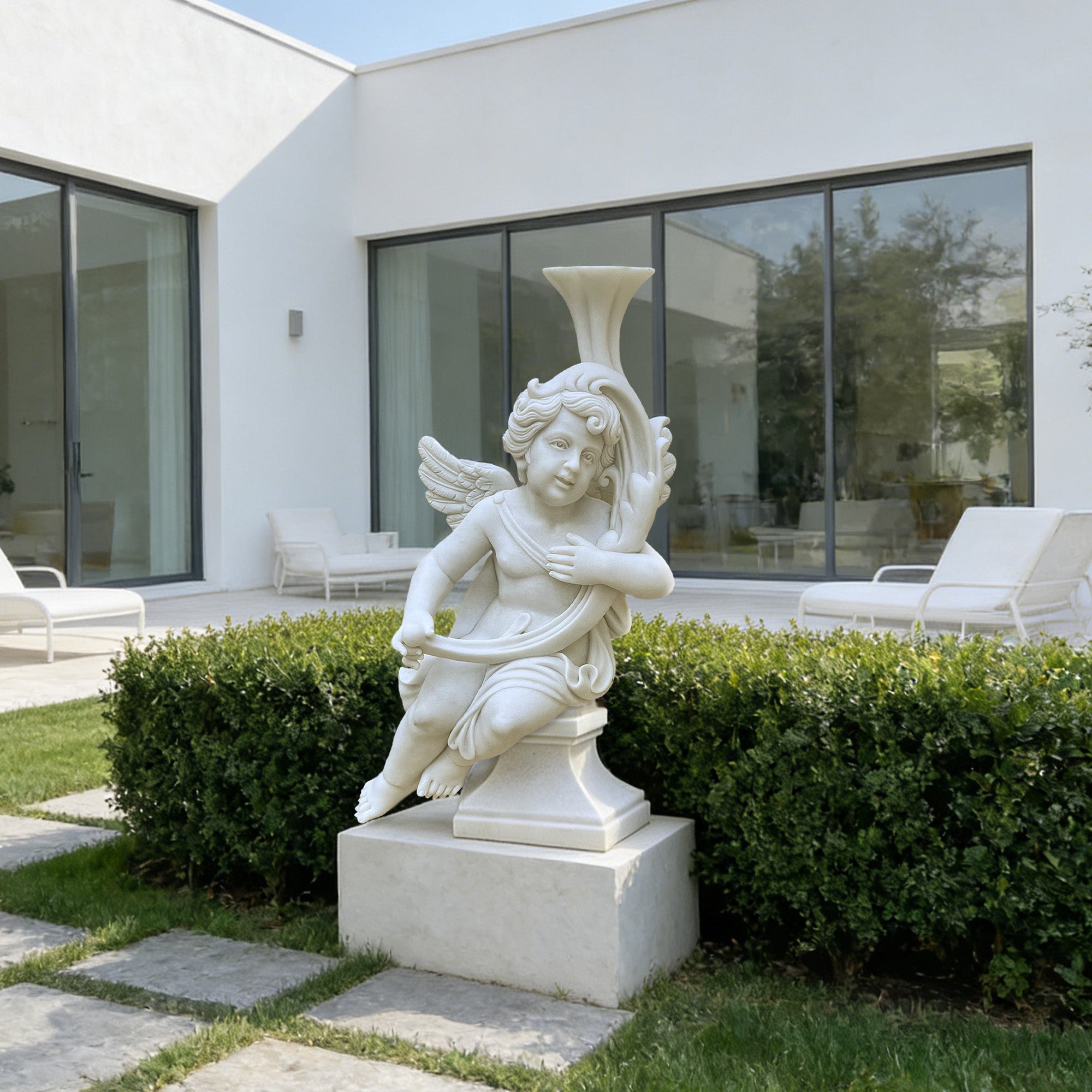 Garden Blessing marble cherub statue installed in a villa courtyard garden, featuring a winged angel figure with cornucopia, white marble finish, pedestal base, lawn, hedges, and modern outdoor setting