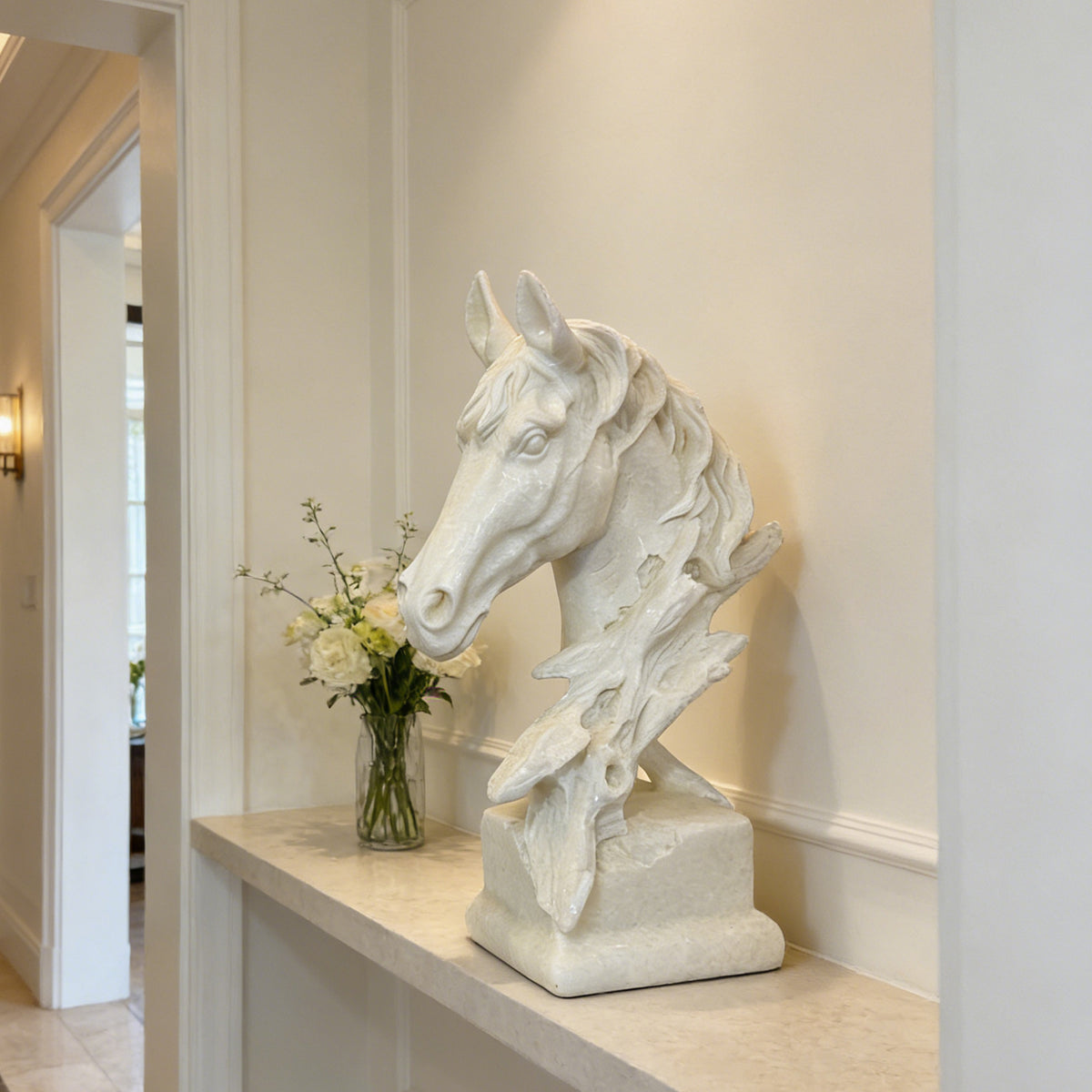 White marble horse head sculpture displayed on a stone console in an elegant residential interior, featuring a detailed flowing mane, upright ears, refined facial carving, and an organic branch-inspired support rising from a rectangular marble pedestal.