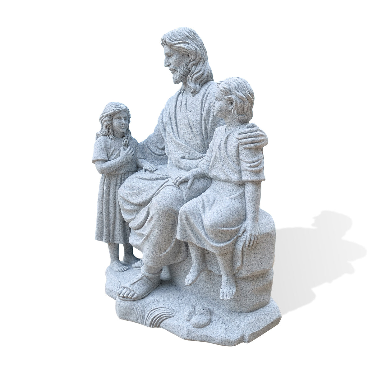 Angled view of a granite Jesus with children statue from the standing girl’s side, highlighting her long carved hair, Jesus’ hand resting across her back and the folds of his robe. The seated boy appears beyond Jesus’ lap, with the group on an irregular base against a white background.