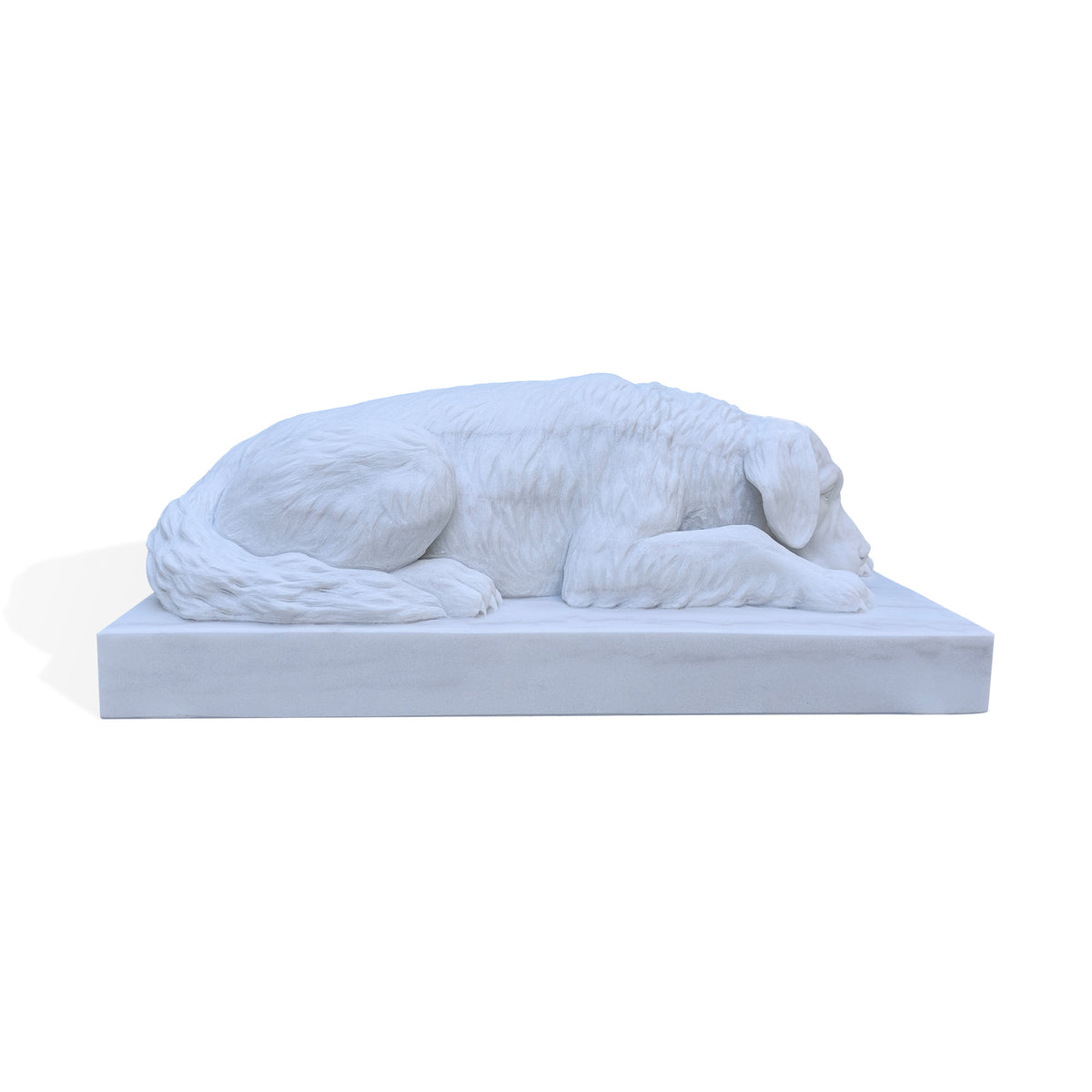 Side profile of a white marble dog statue in a relaxed lying pose, showing its long body, lowered head, floppy ear, extended front leg and curled tail. Carved fur contrasts with the smooth rectangular base against a white background.