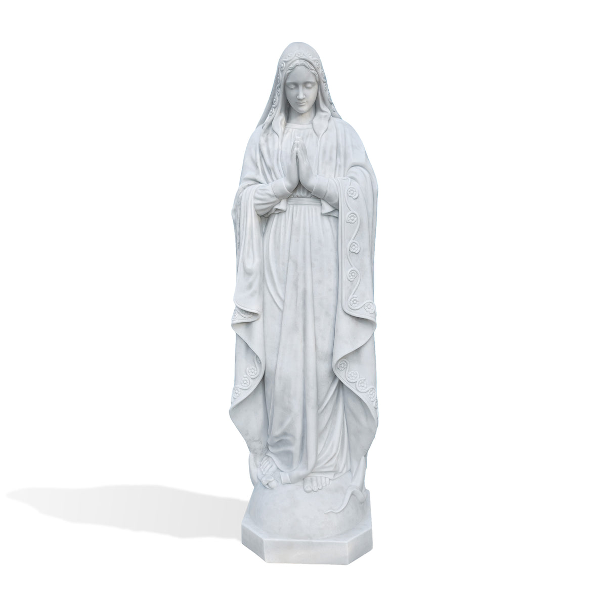 Full front view of a white marble praying Virgin Mary statue with downcast eyes, joined palms and a belted robe beneath a flowing mantle decorated with carved flowers and vines. Bare feet and a curved serpent-like detail appear on the rounded support above a faceted base.