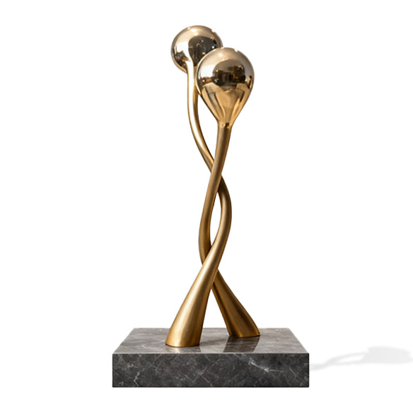 Gold abstract sculpture on a marble base against a white background