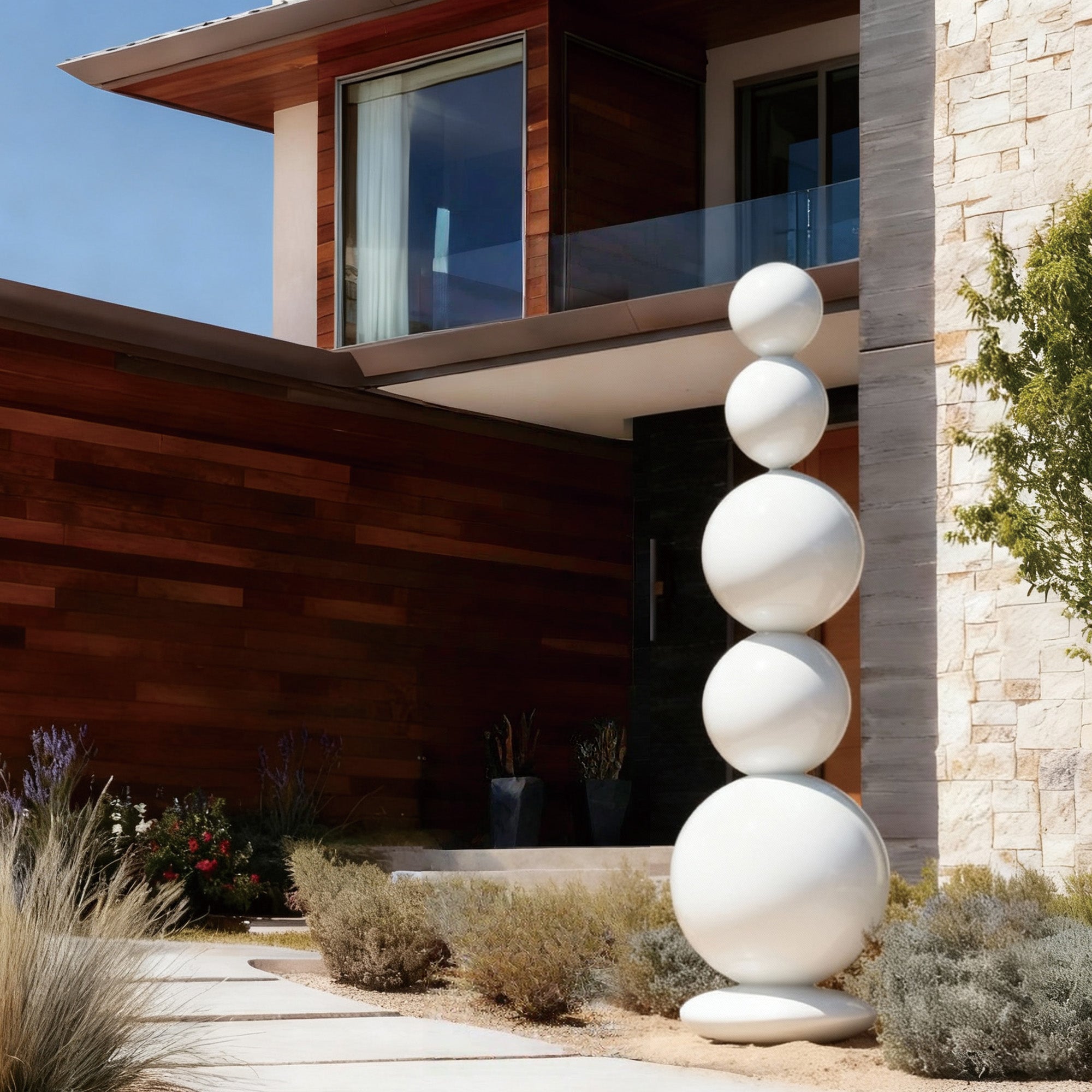 White stainless steel stacked spheres sculpture displayed in the outdoor entrance of a modern estate, surrounded by landscaping.