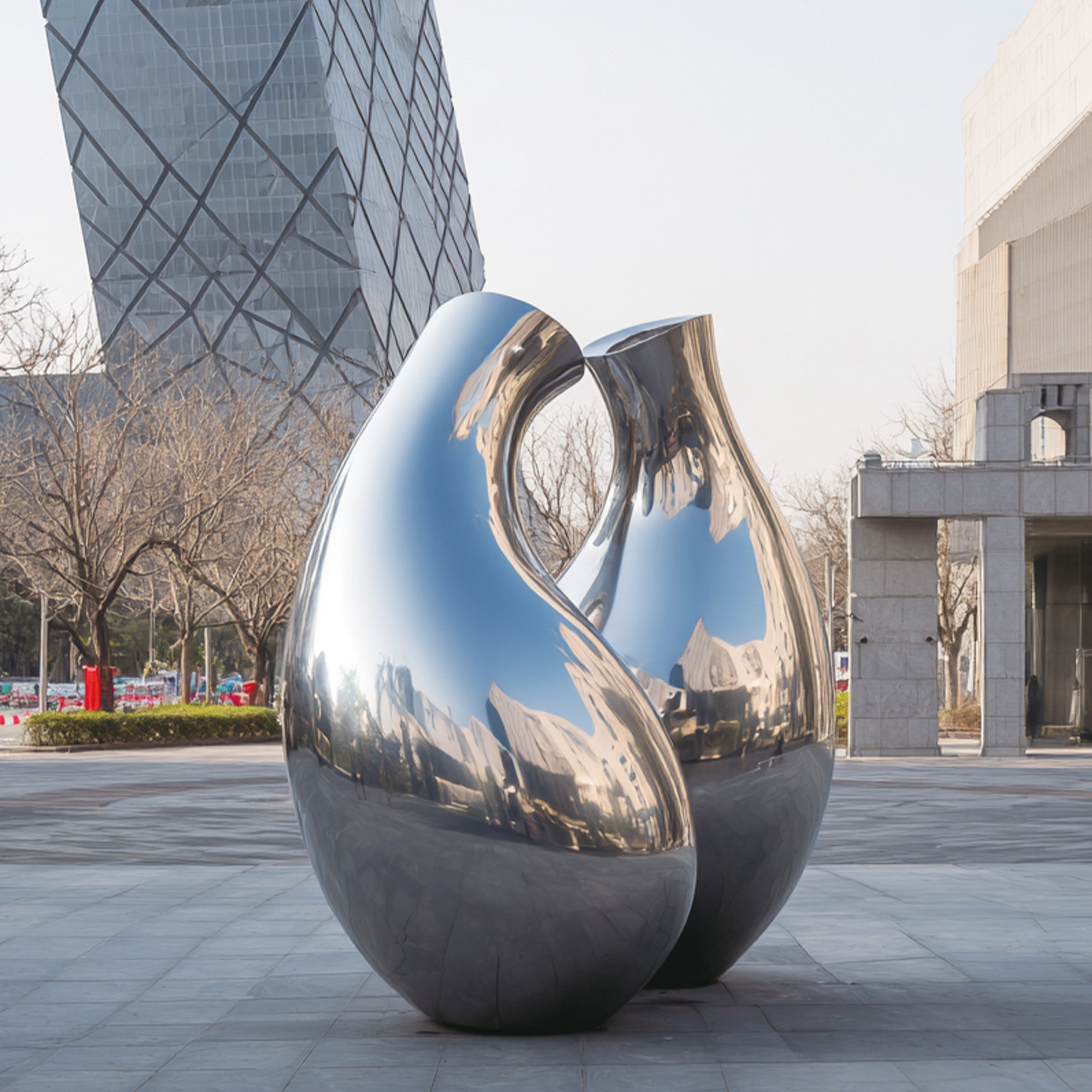 Two reflective metal sculptures in an urban setting with modern buildings.