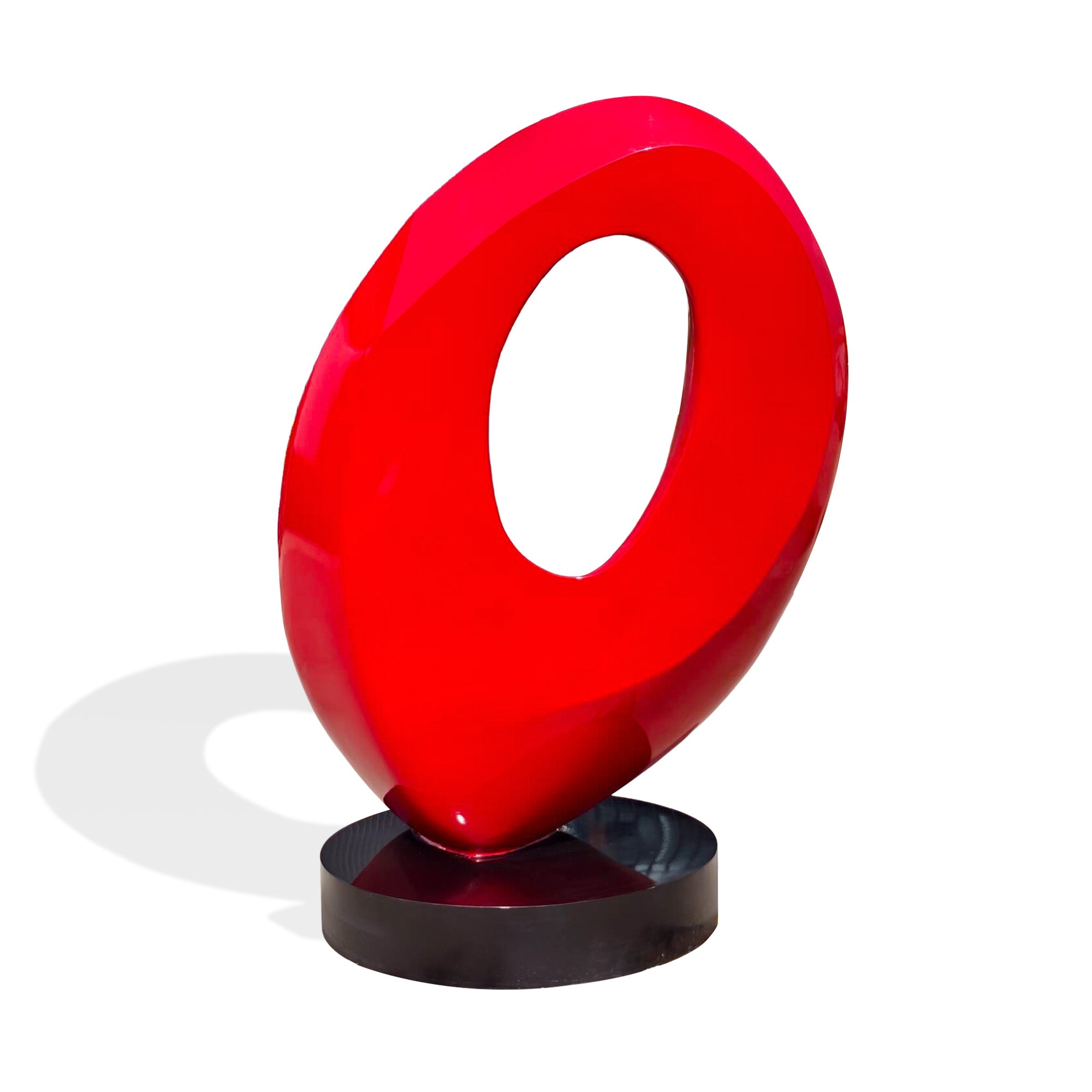 Back view of glossy red painted stainless steel abstract ring sculpture with oval center cutout, modern statement art on black round base.