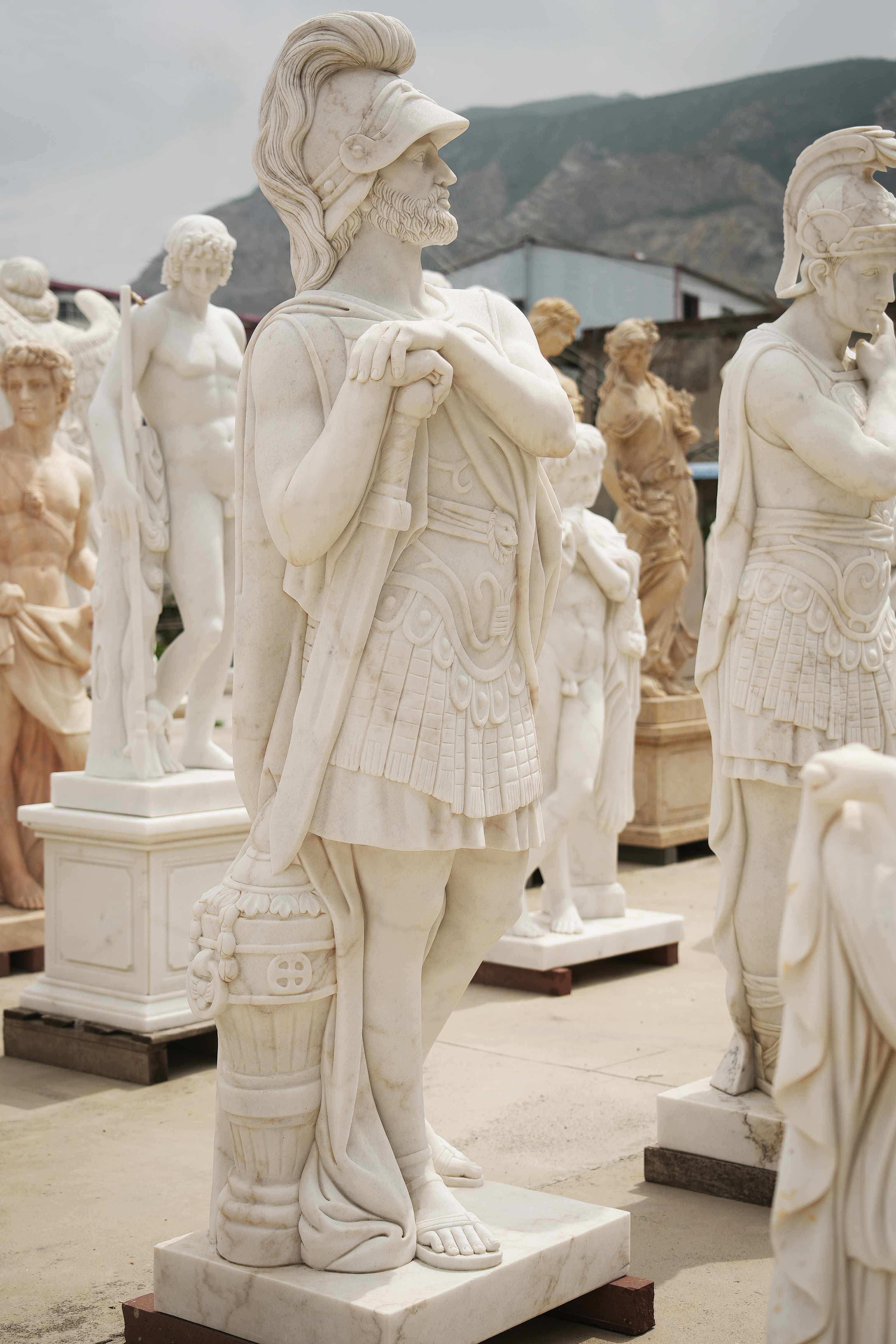 Marble statue of a Roman warrior with detailed armor, standing confidently among other classical sculptures in an outdoor setting