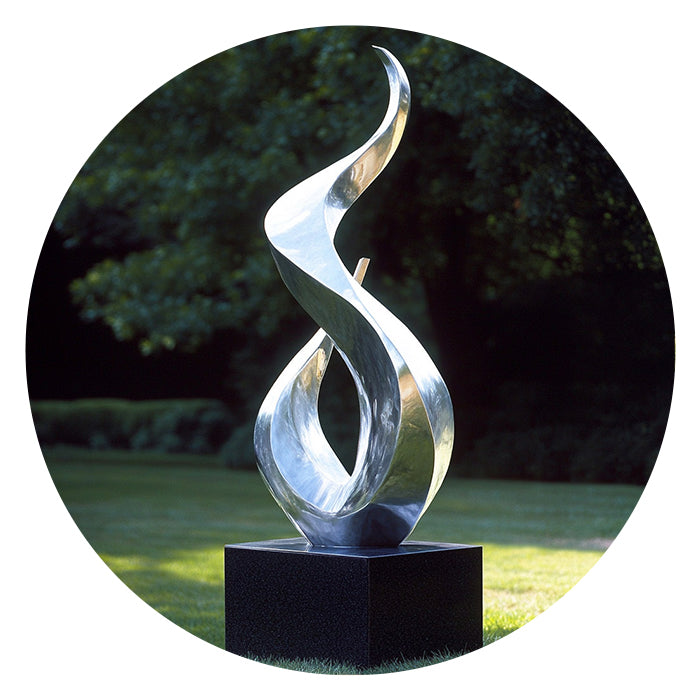 Abstract metal sculpture on a black pedestal against a blurred natural background