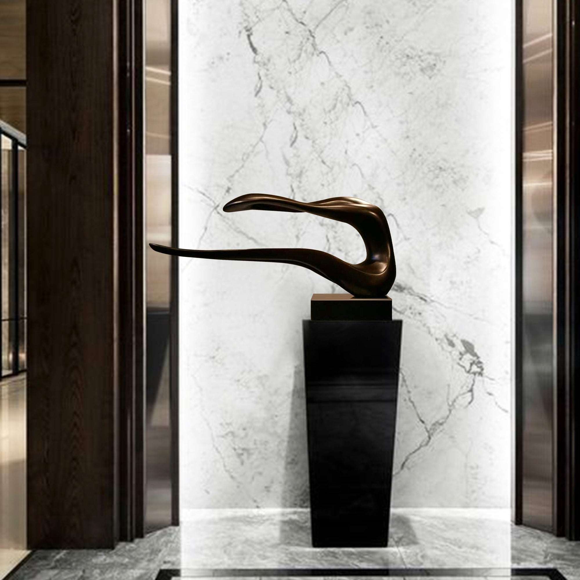 A sleek, abstract bronze sculpture with elongated, flowing curves, mounted on a black pedestal, set against a marble background in a modern interior space