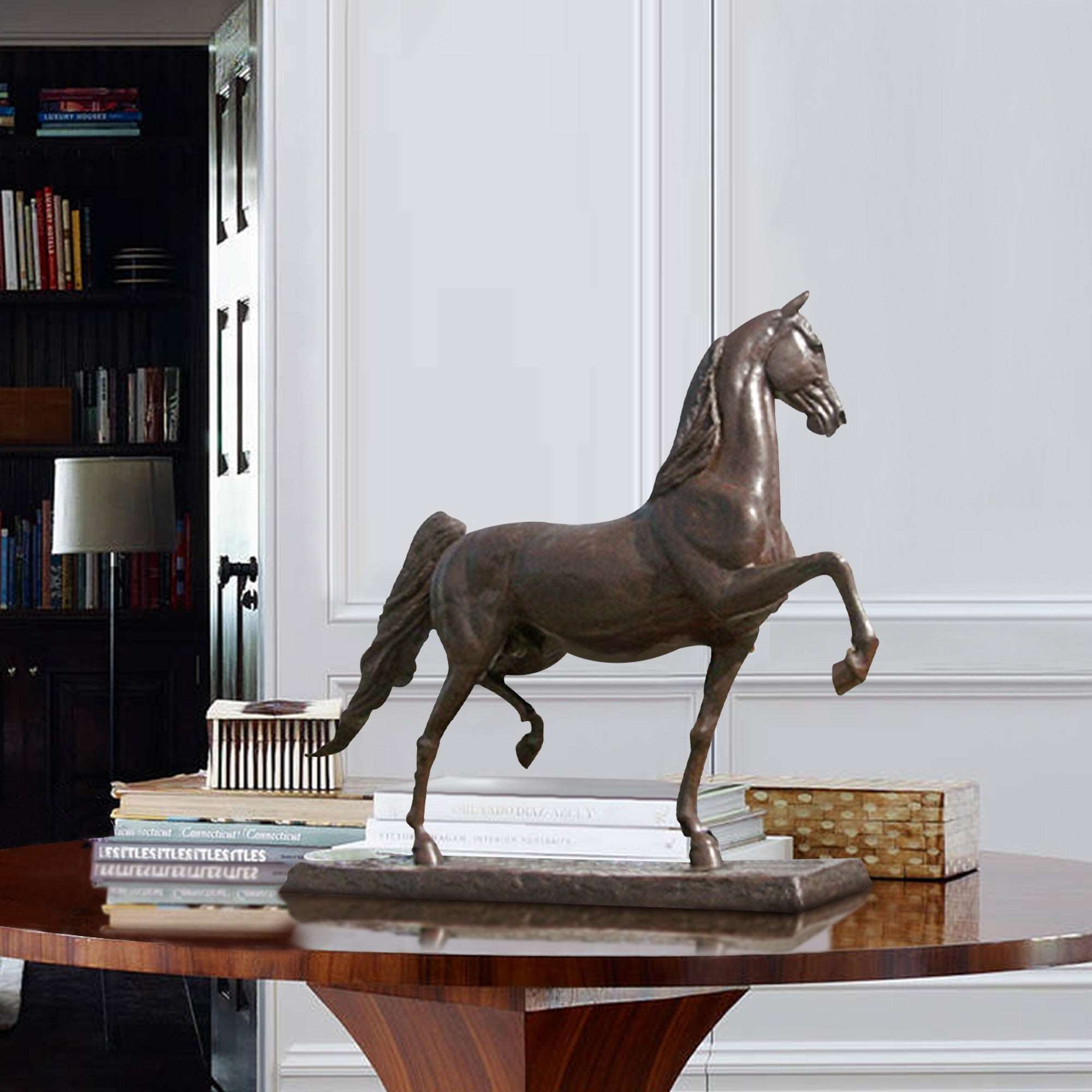 Bronze statue of a horse in a trotting pose, displayed on a table in a refined interior setting with books and decor