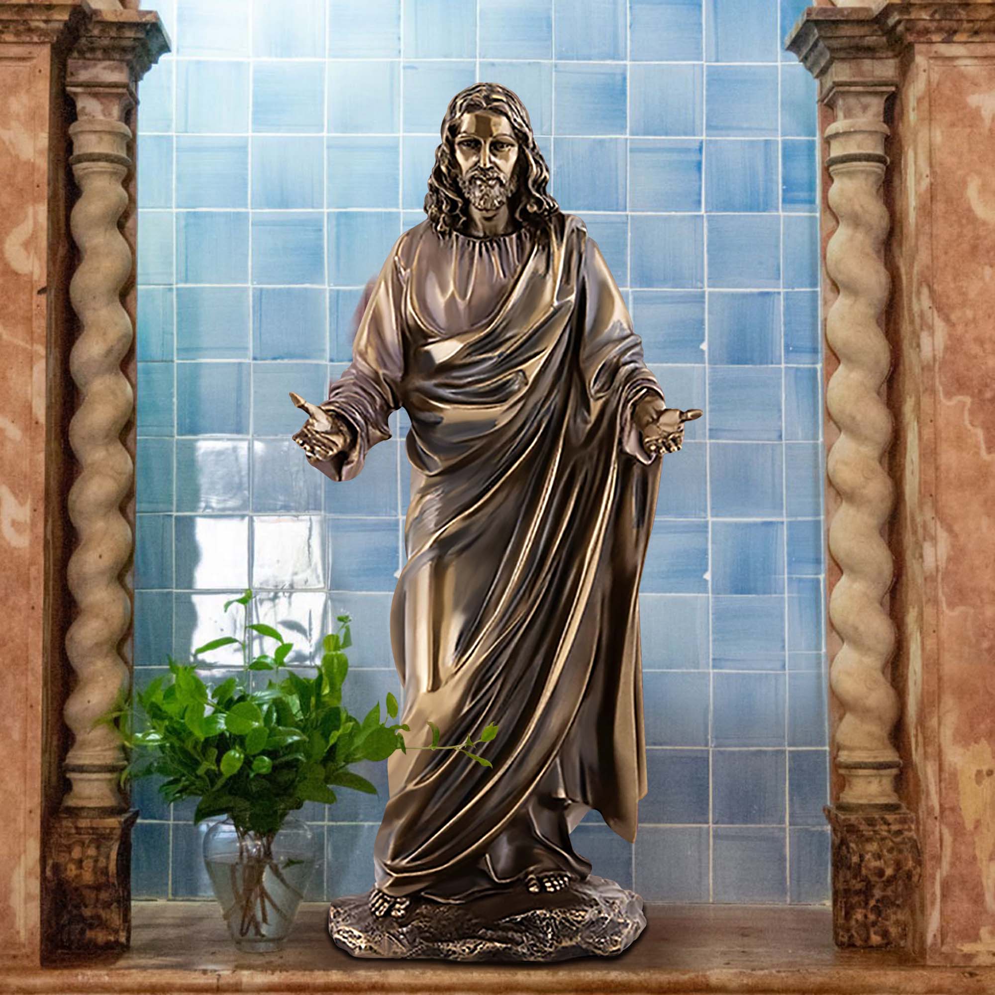 Bronze statue of Jesus Christ with outstretched arms, displayed in a religious setting with a blue tiled background.