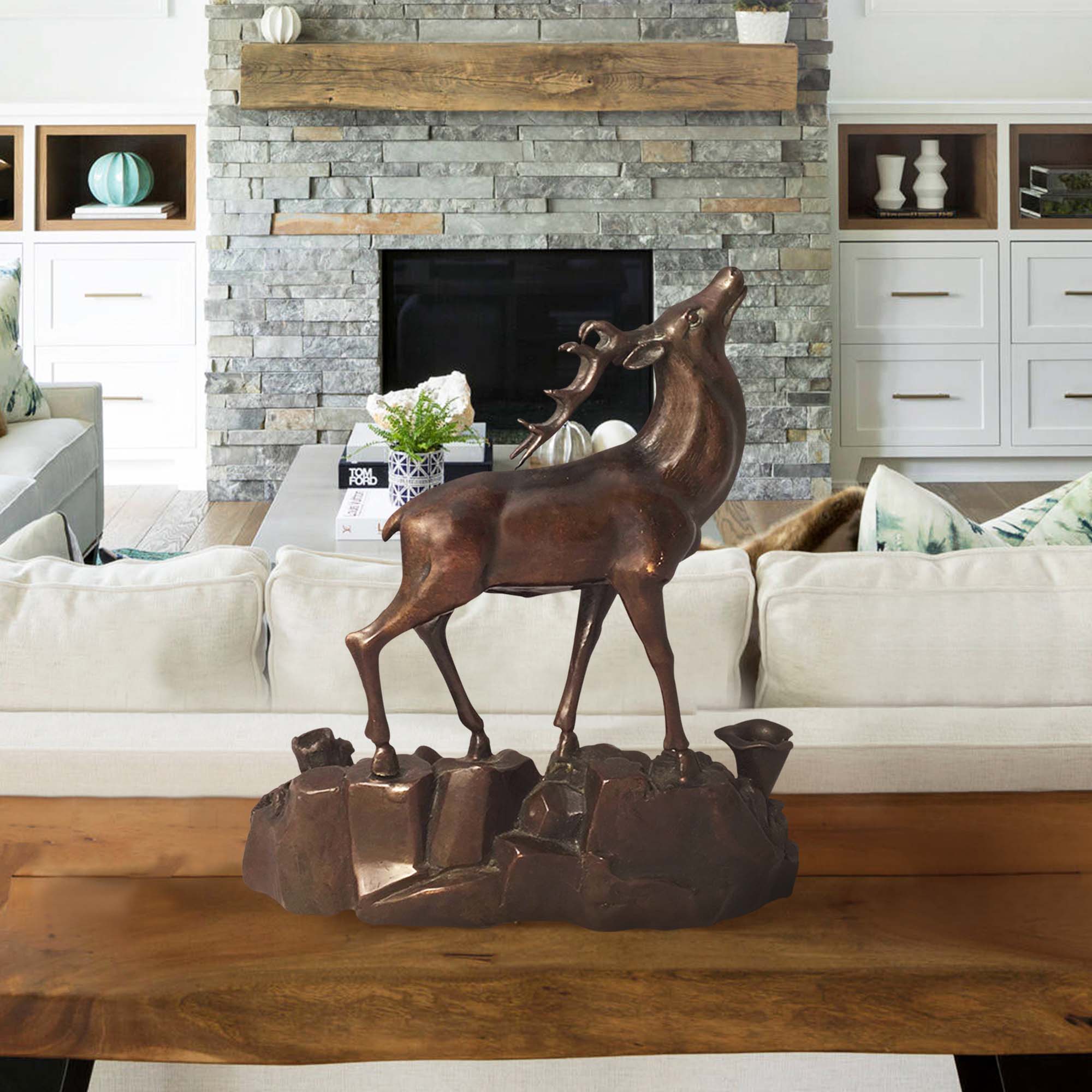 Bronze sculpture of a majestic stag standing on rocky terrain, displayed in a rustic living room setting