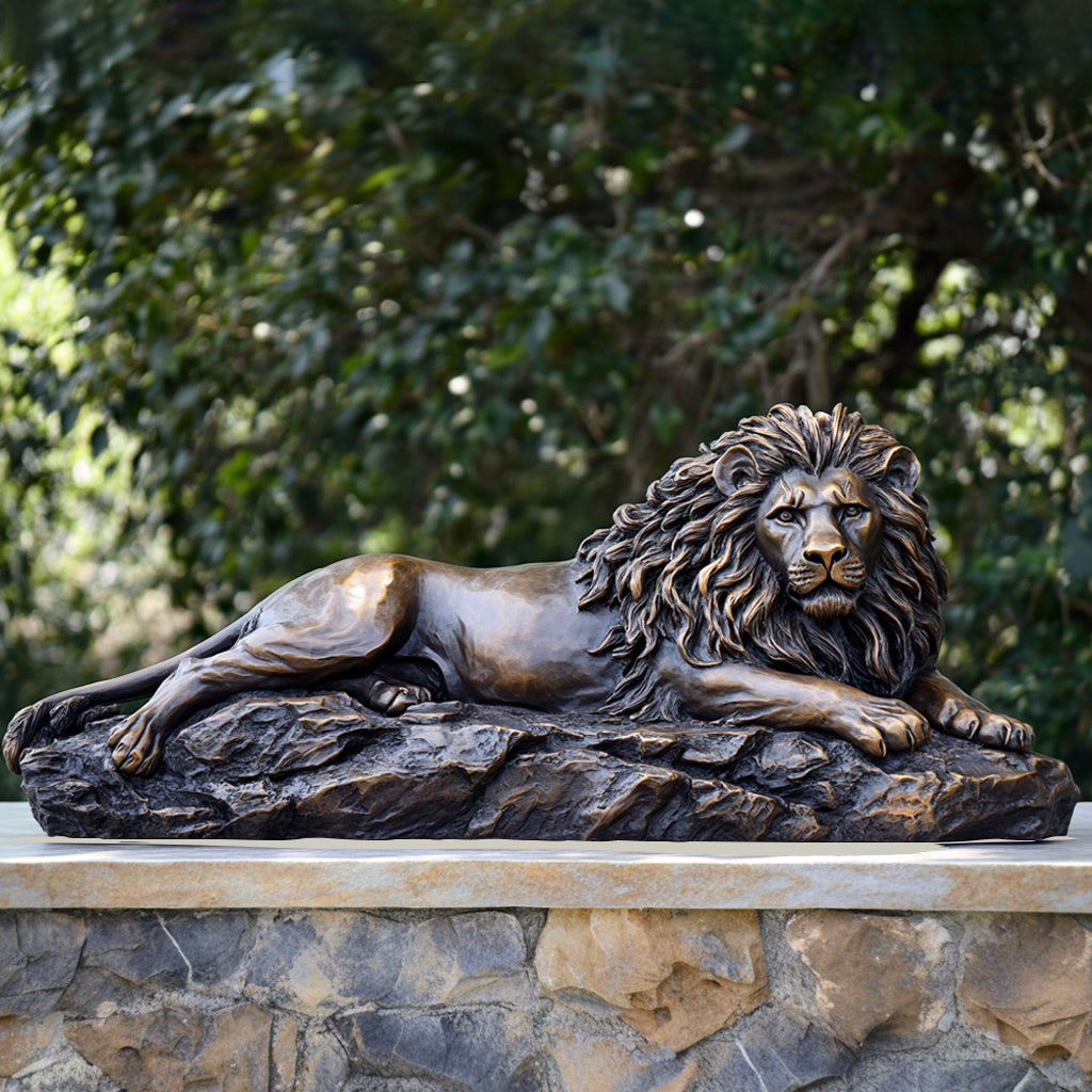 Majestic Reclining Bronze Lion Sculpture with a classic bronze finish, resting on a rocky base, display in garden