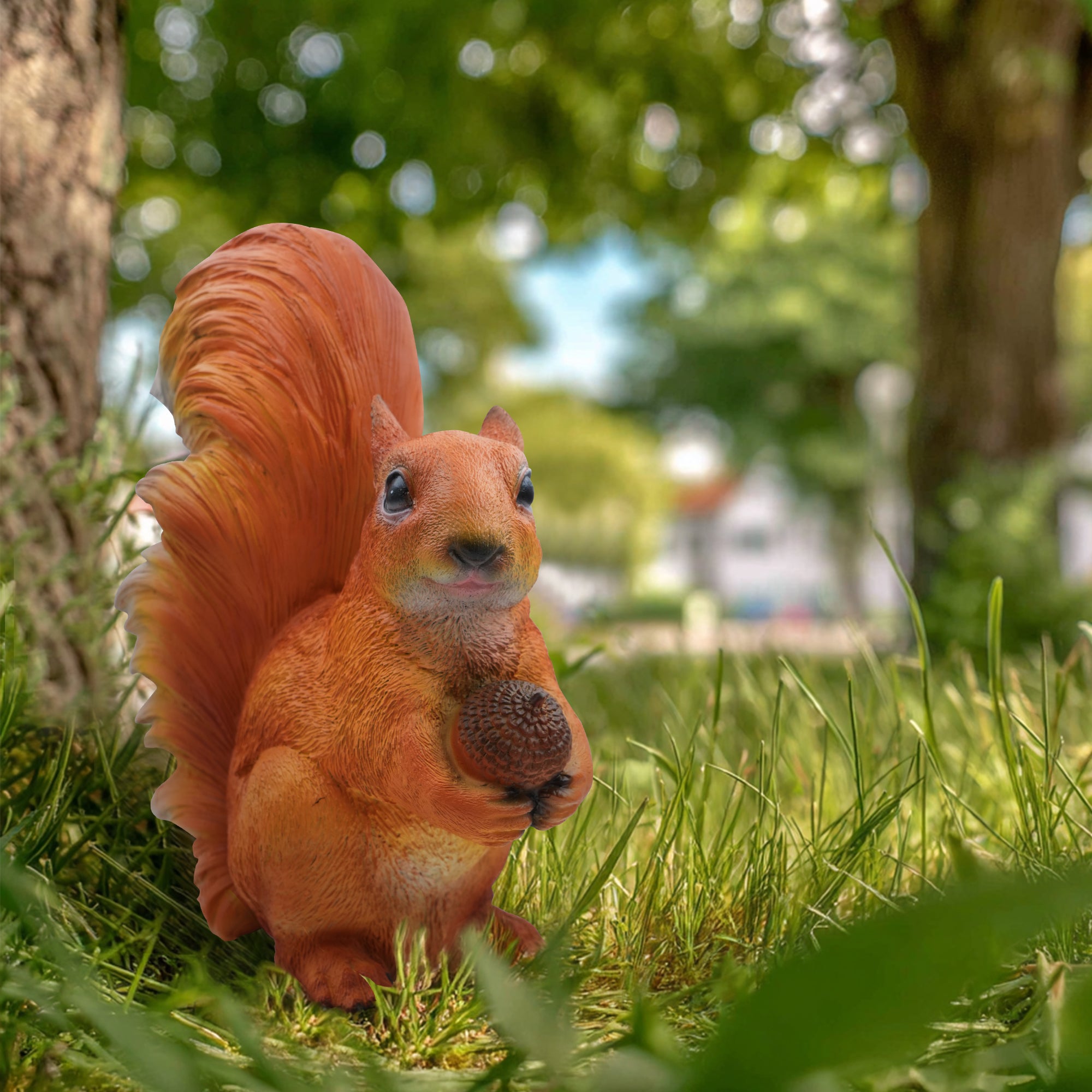 Cute bronze squirrel garden sculpture with acorn, surrounded by green grass, featuring realistic fur and expressive eyes 