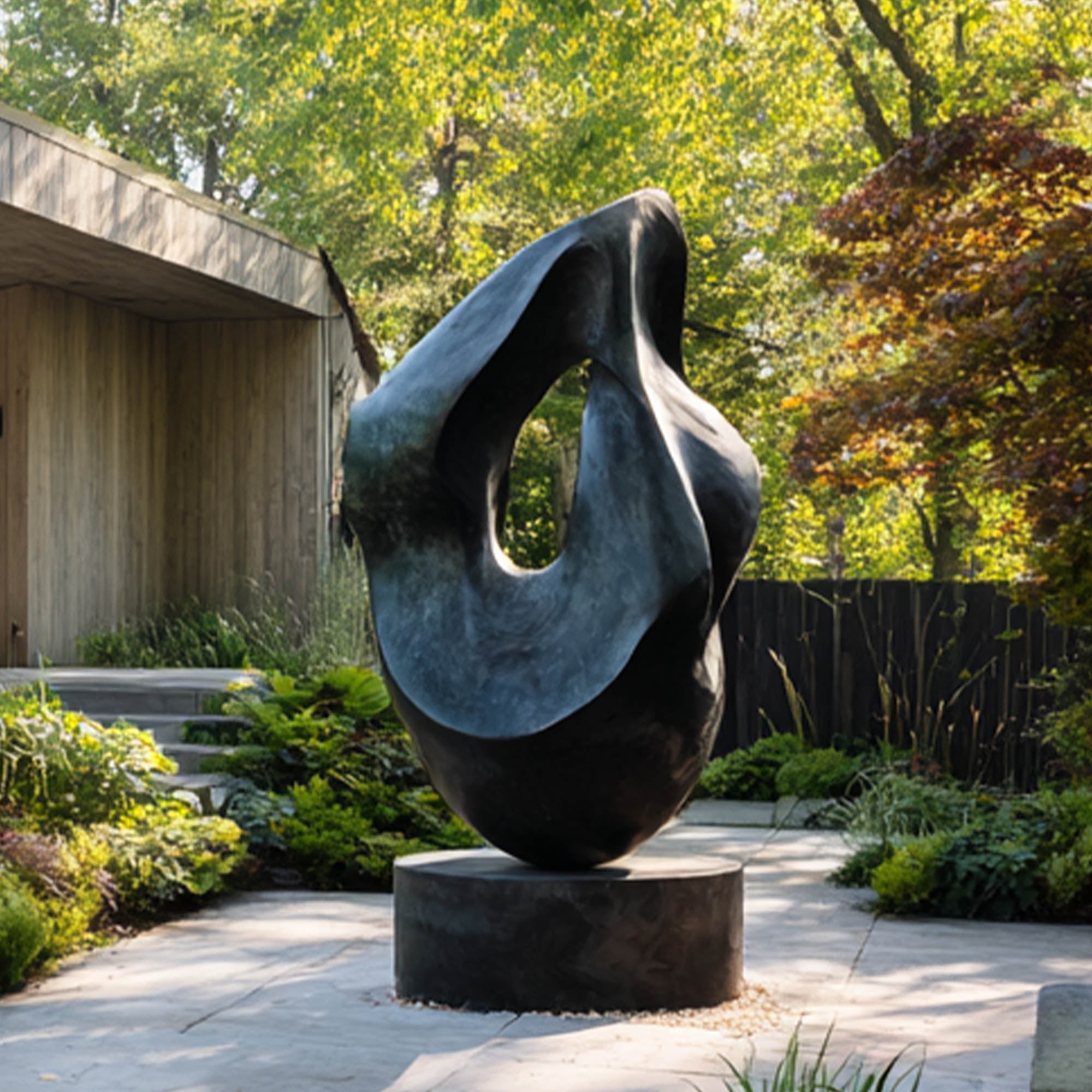 Abstract bronze sculpture in a garden setting with trees and a building in the background