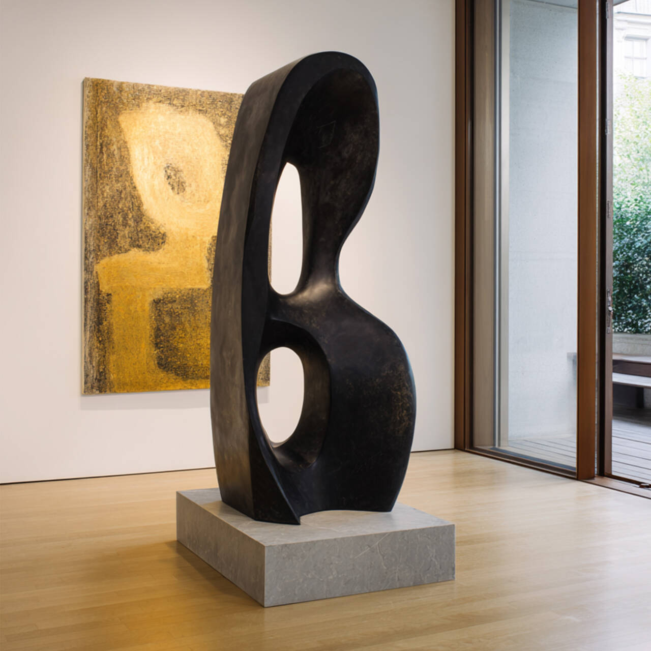 Abstract sculpture on a pedestal in an indoor setting with a painting in the background
