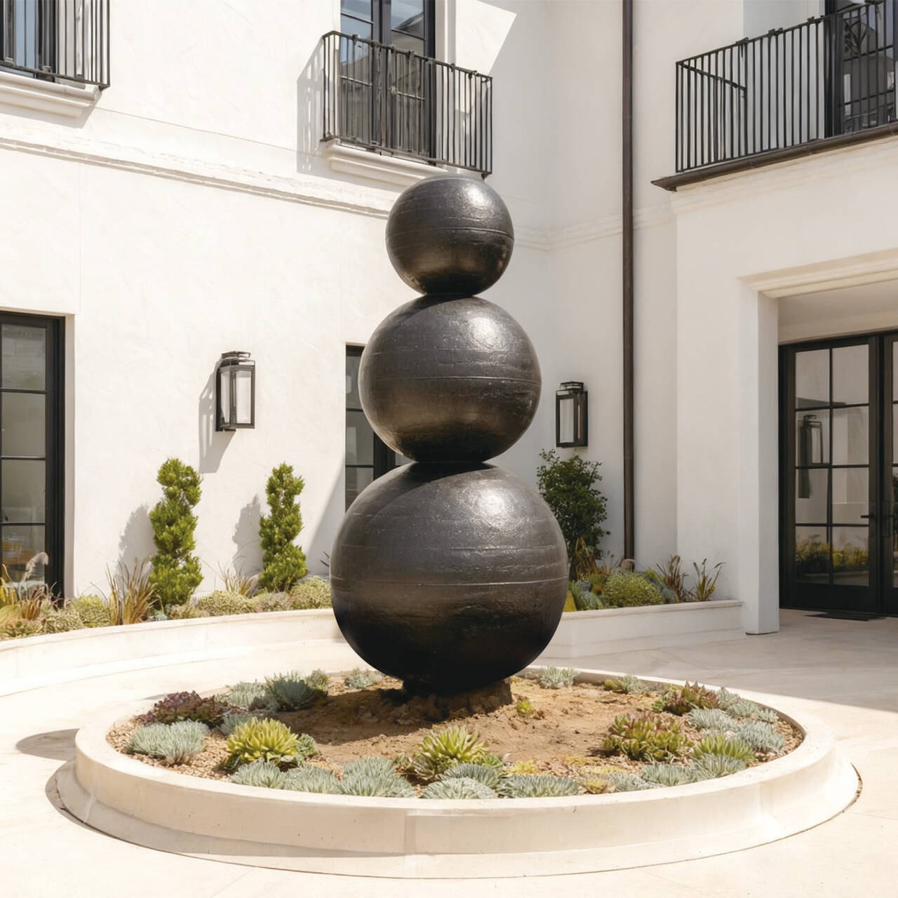 Decorative outdoor sculpture of stacked spheres in a garden setting with a building in the background.