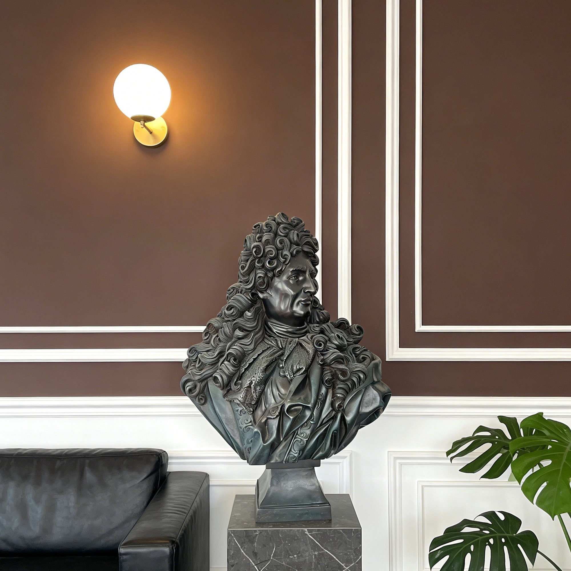 Bronze bust of a man on a pedestal in a room with brown walls and a black sofa.