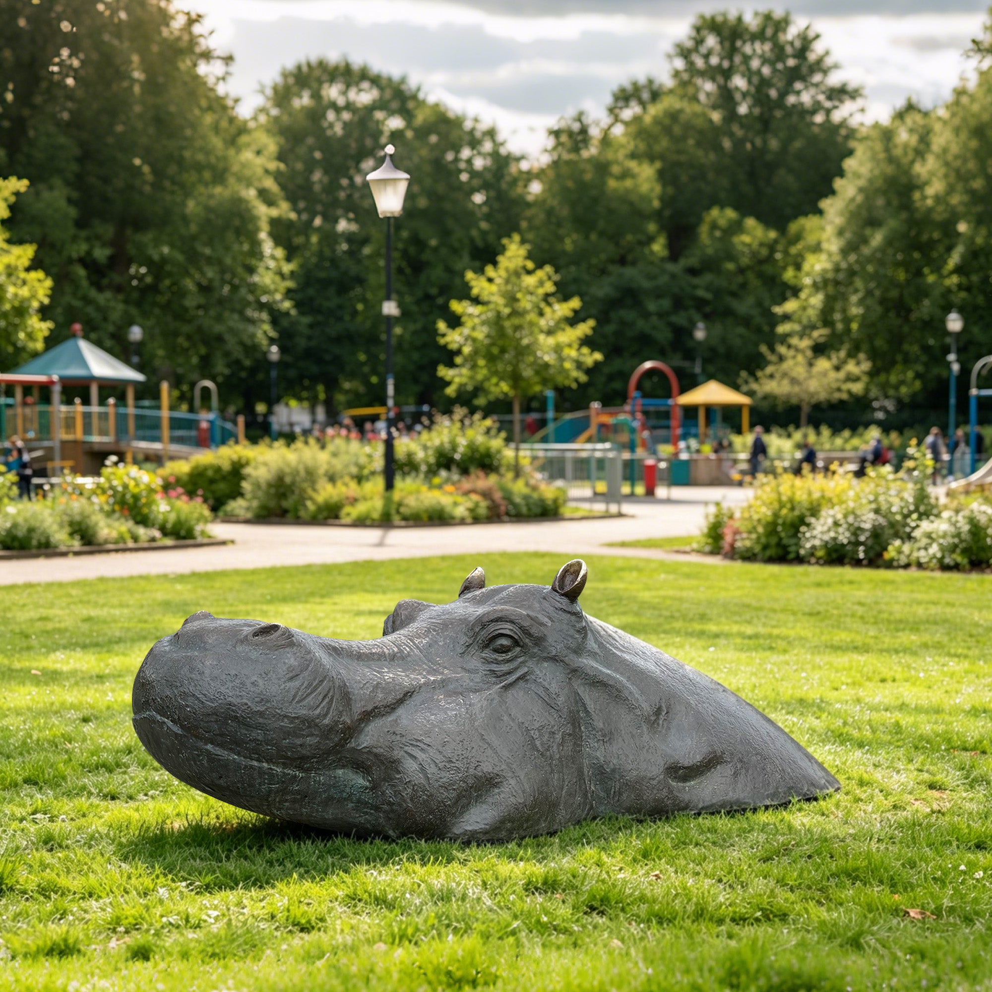 A bronze hippopotamus statue displayed on a public park lawn with a closed mouth, raised eyes, small ears, textured skin, and a low partially submerged body form.