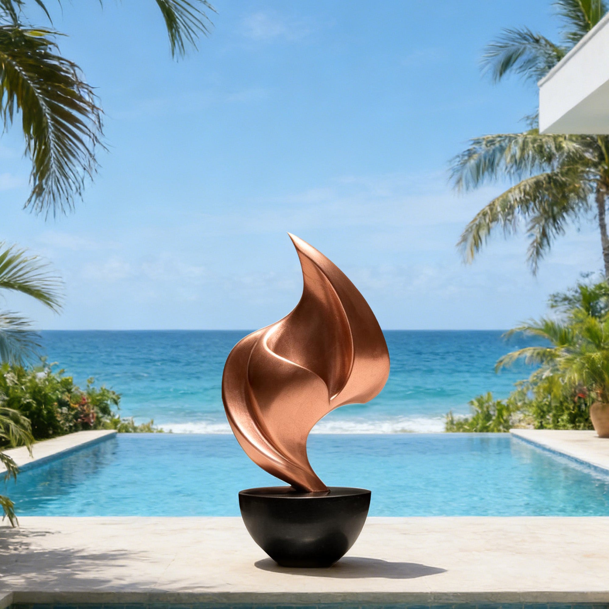 Bronze abstract flame sculpture displayed beside an oceanfront pool with a copper bronze finish, flowing leaf-like form, black bowl base, and tropical resort setting.