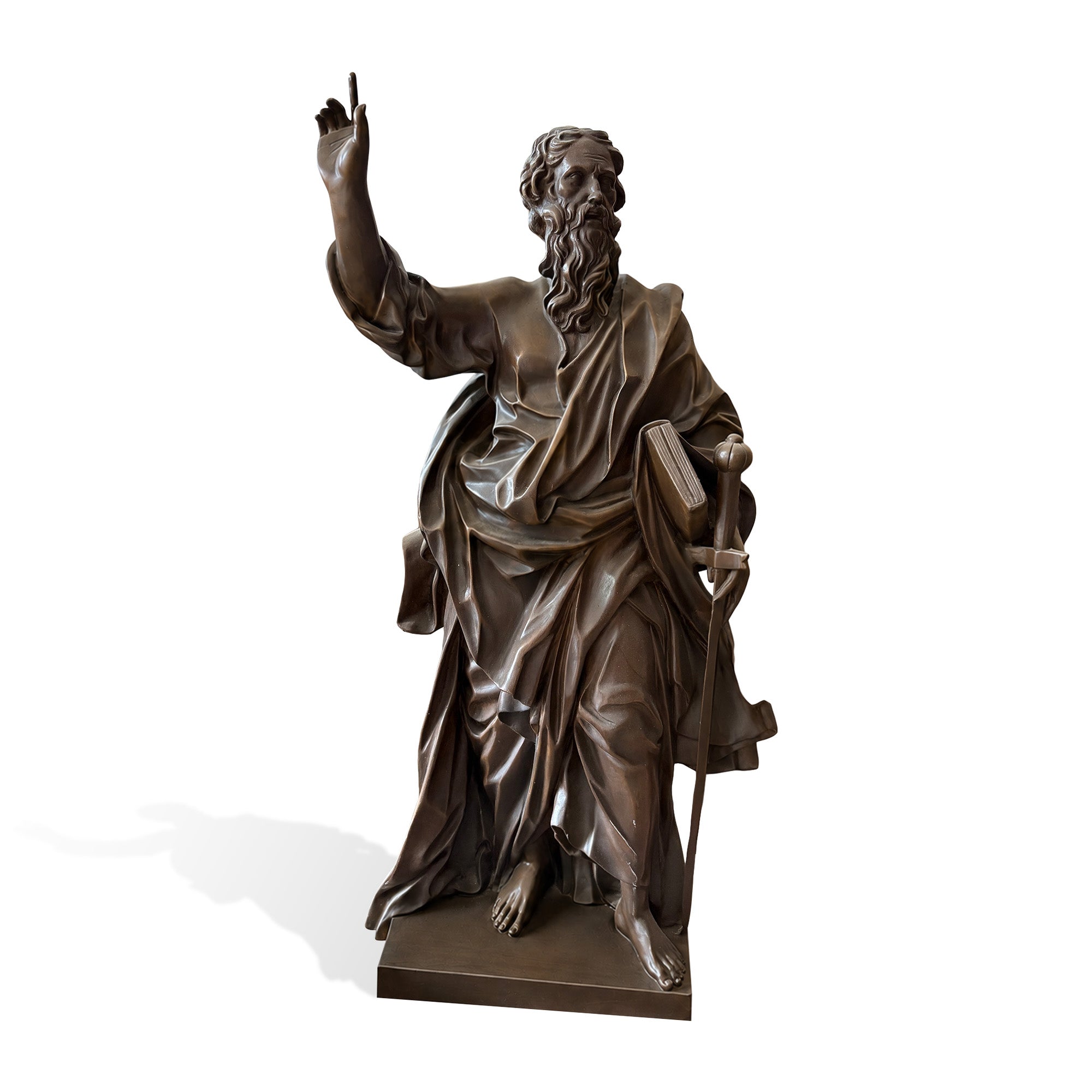 Side three-quarter view of a bronze Saint Paul Apostle statue with raised hand, long beard, flowing robe, book, sword, and rectangular base on a light background.
