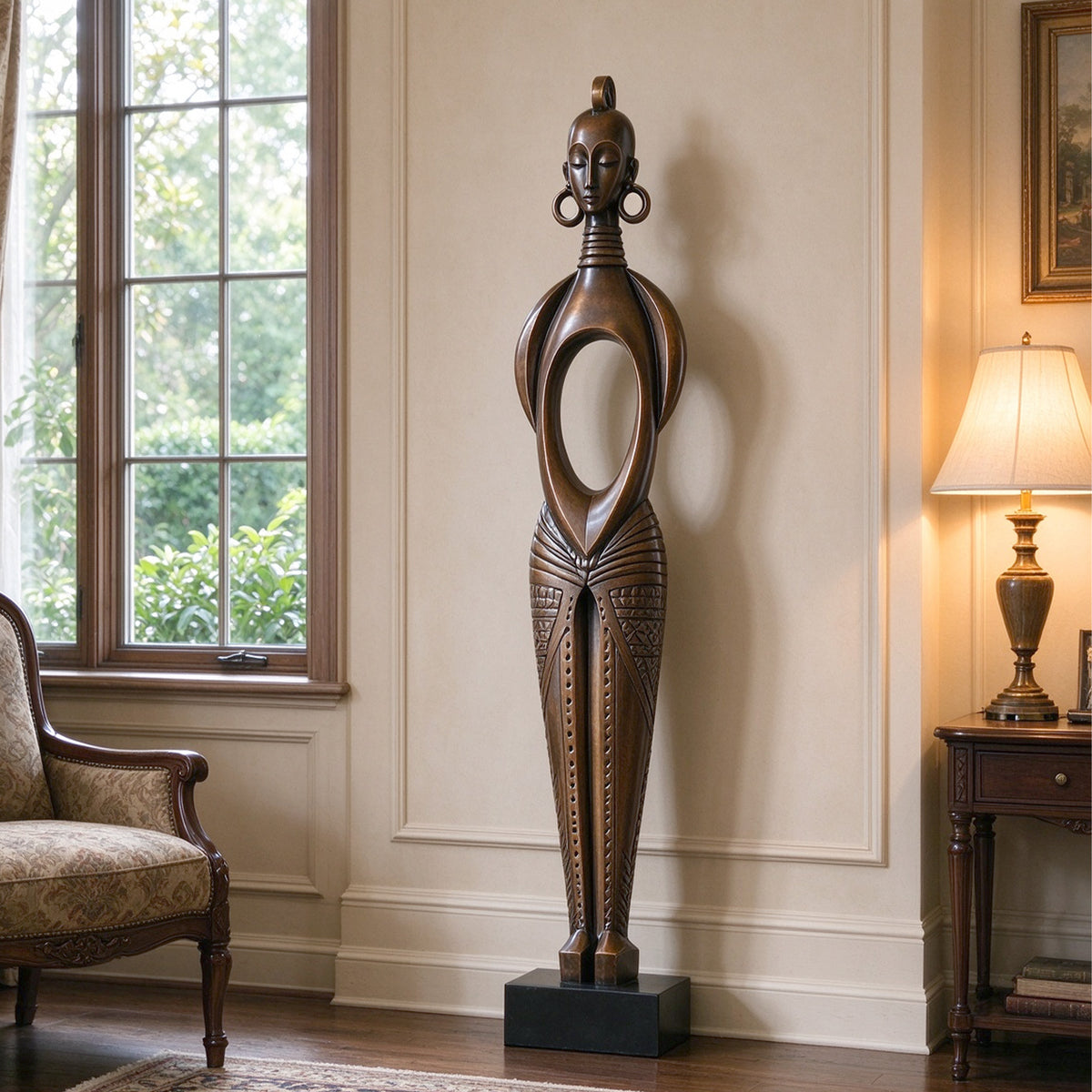 Abstract bronze female figure sculpture with a slender silhouette, oval torso opening, and antique brown finish, displayed on a black base in an elegant living room beside a window and armchair.