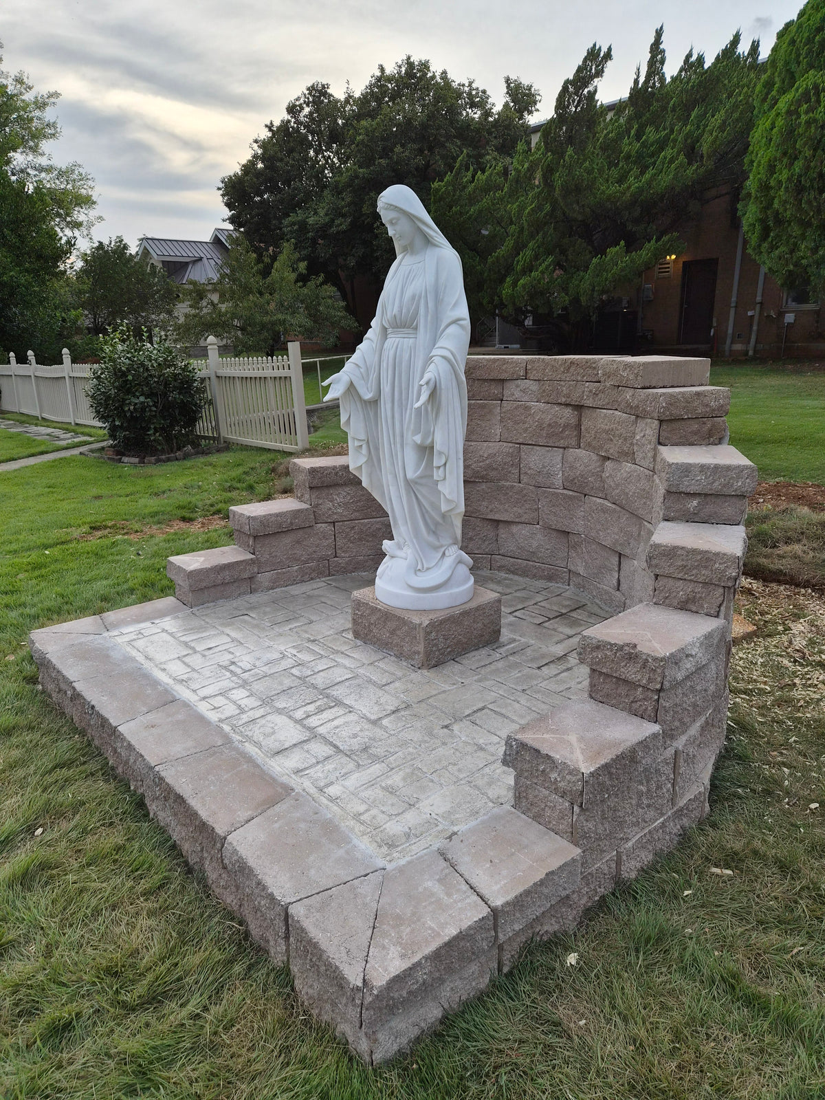 Our Lady of Grace marble statue with open hands installed in an outdoor church garden