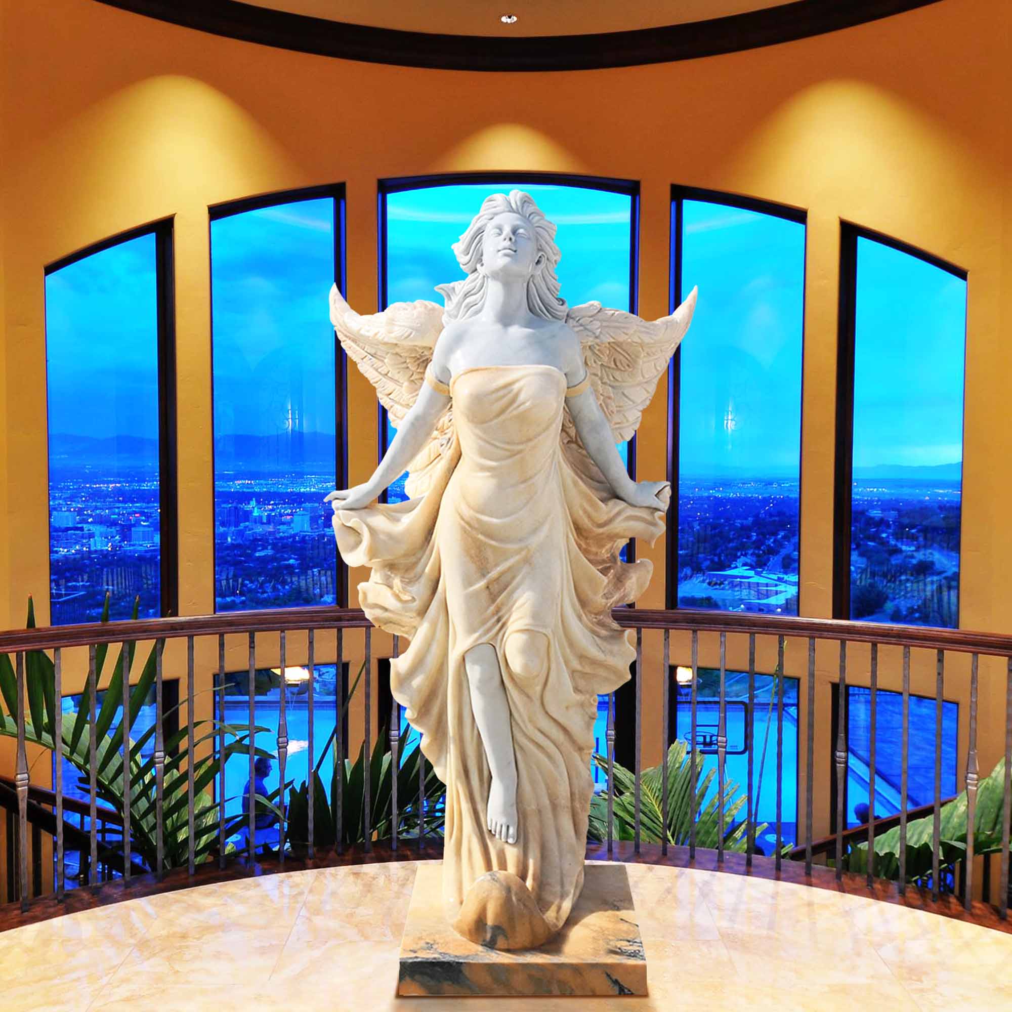 Golden angel marble statue with flowing robes and wings, displayed in a luxurious setting with large windows.