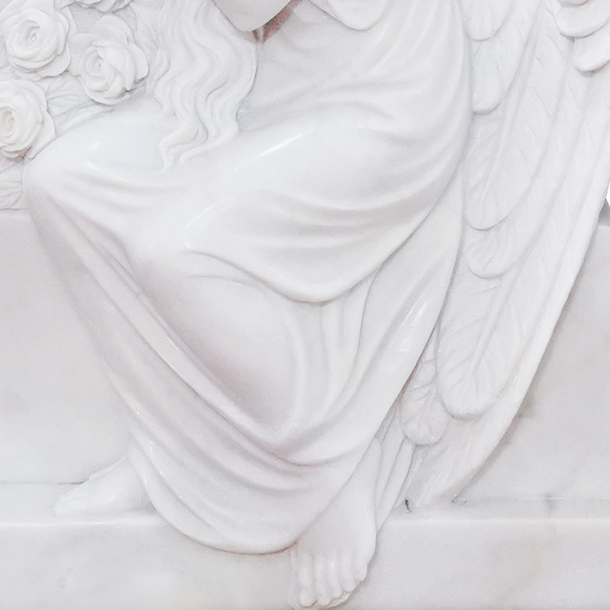 close up of marble angel headstone showing carved feet flowing robe and roses detail