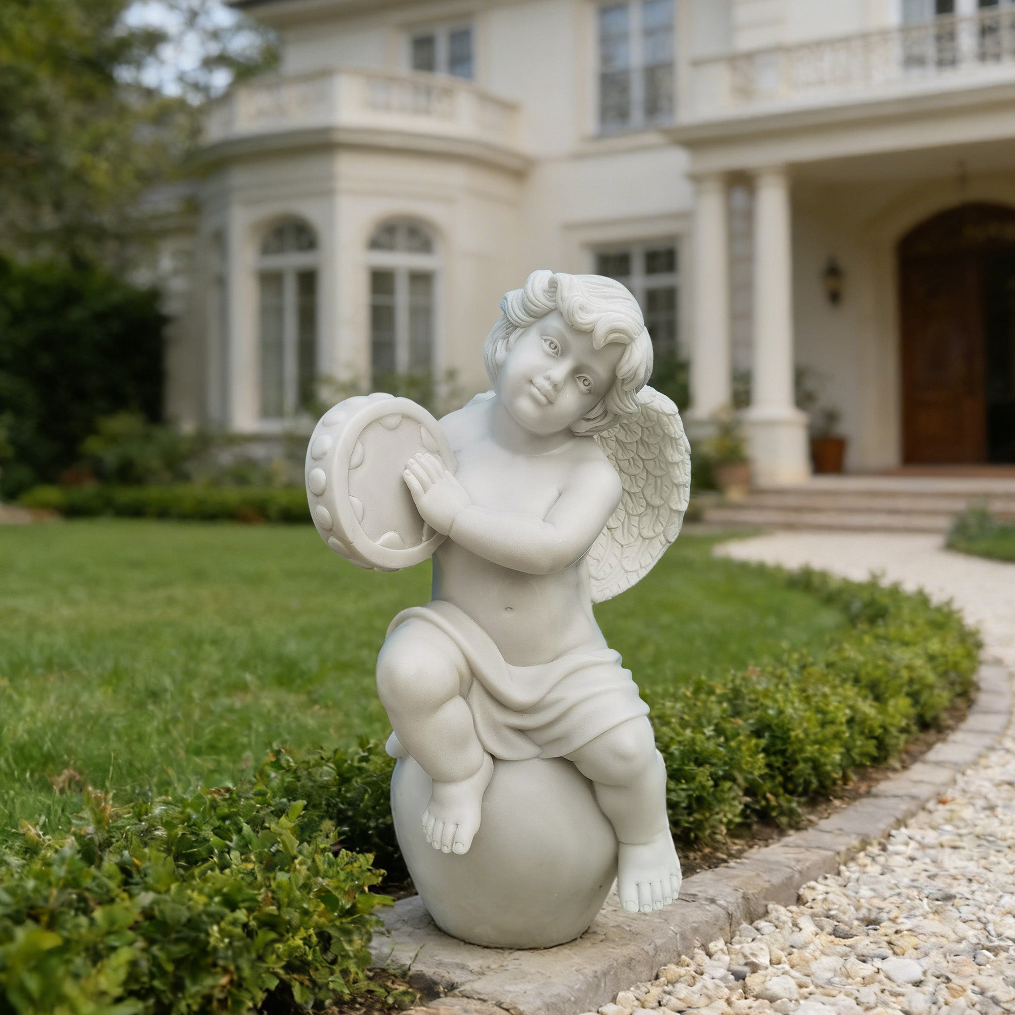 white natural marble musical cherub statue with tambourine displayed beside garden pathway in front of classical villa landscape