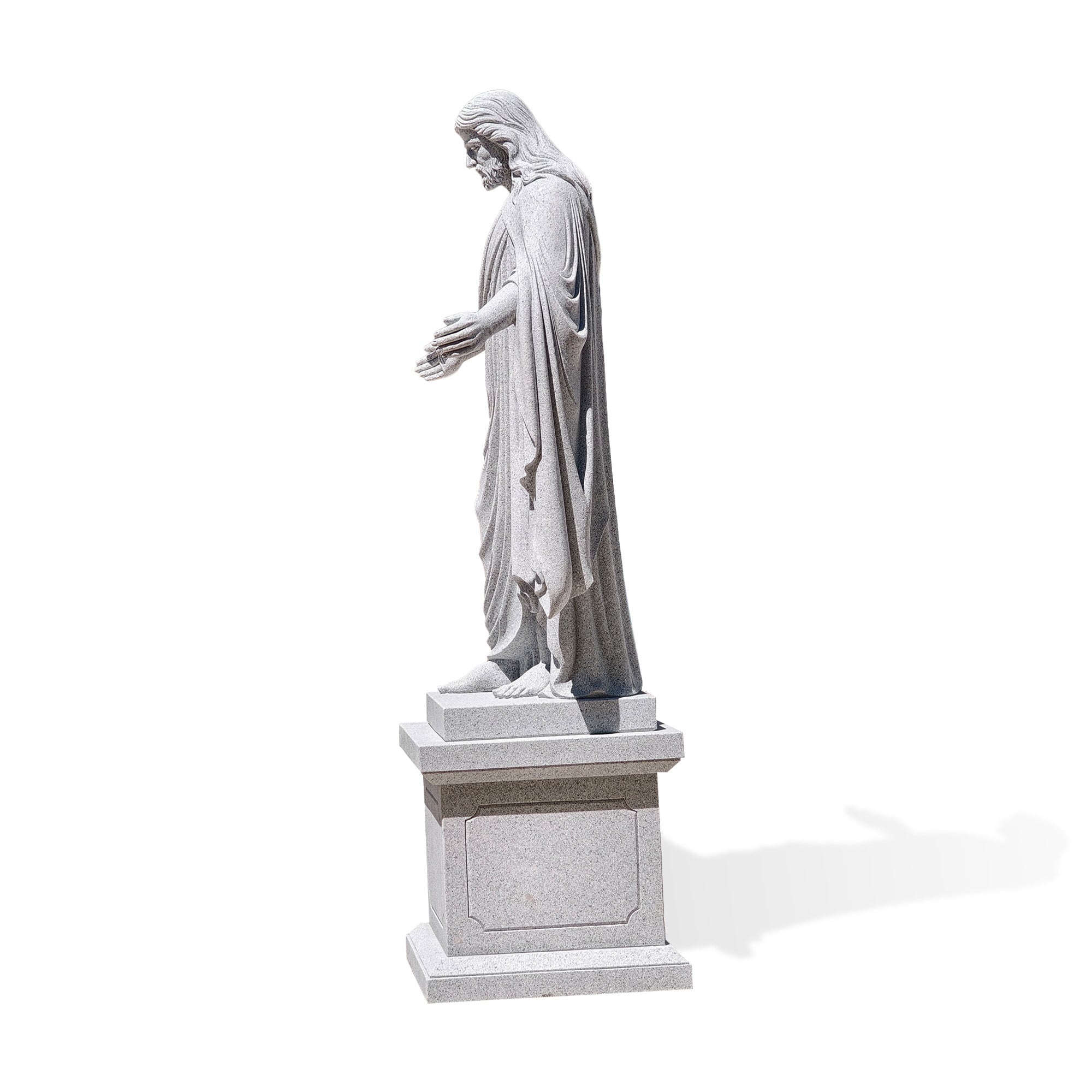 Side view of a hand carved grey granite Jesus with open arms statue on a matching stone pedestal.
