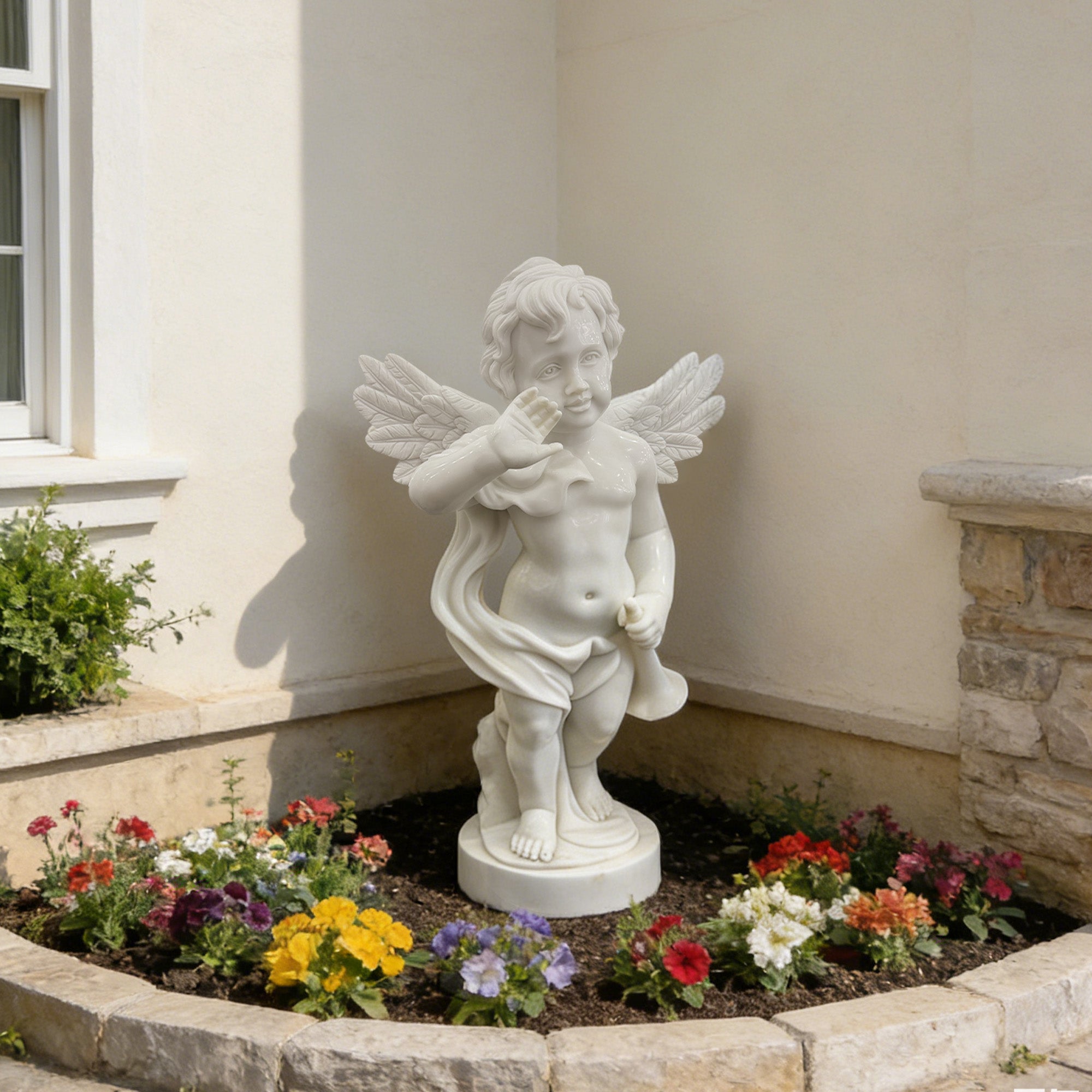 Herald of Grace white marble cherub statue holding a trumpet, featuring winged angel figure, raised hand, carved feather wings, round base, and flower bed garden setting