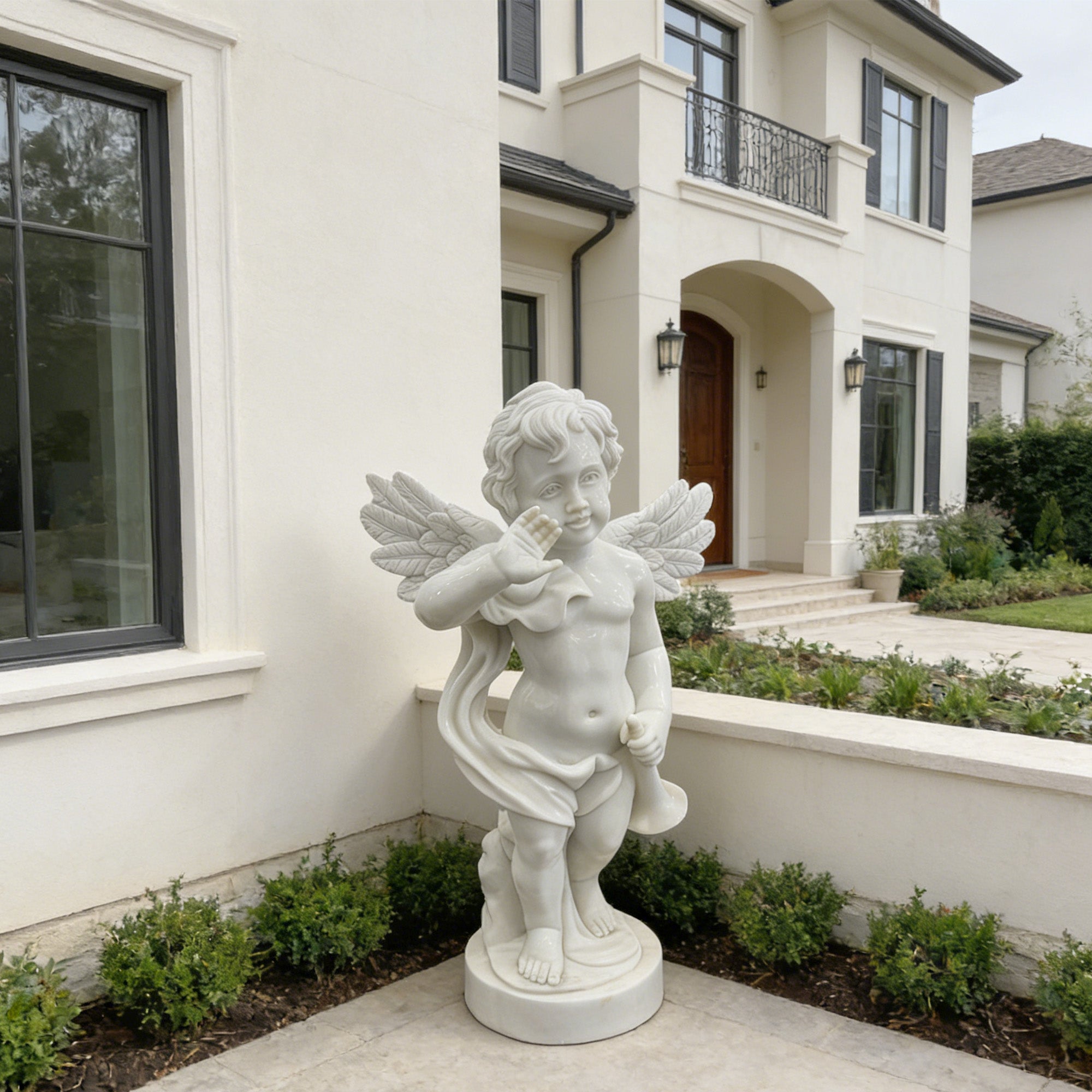 White marble cherub angel statue with trumpet installed in a villa courtyard, featuring raised blessing hand, detailed wings, round base, and luxury garden entrance setting