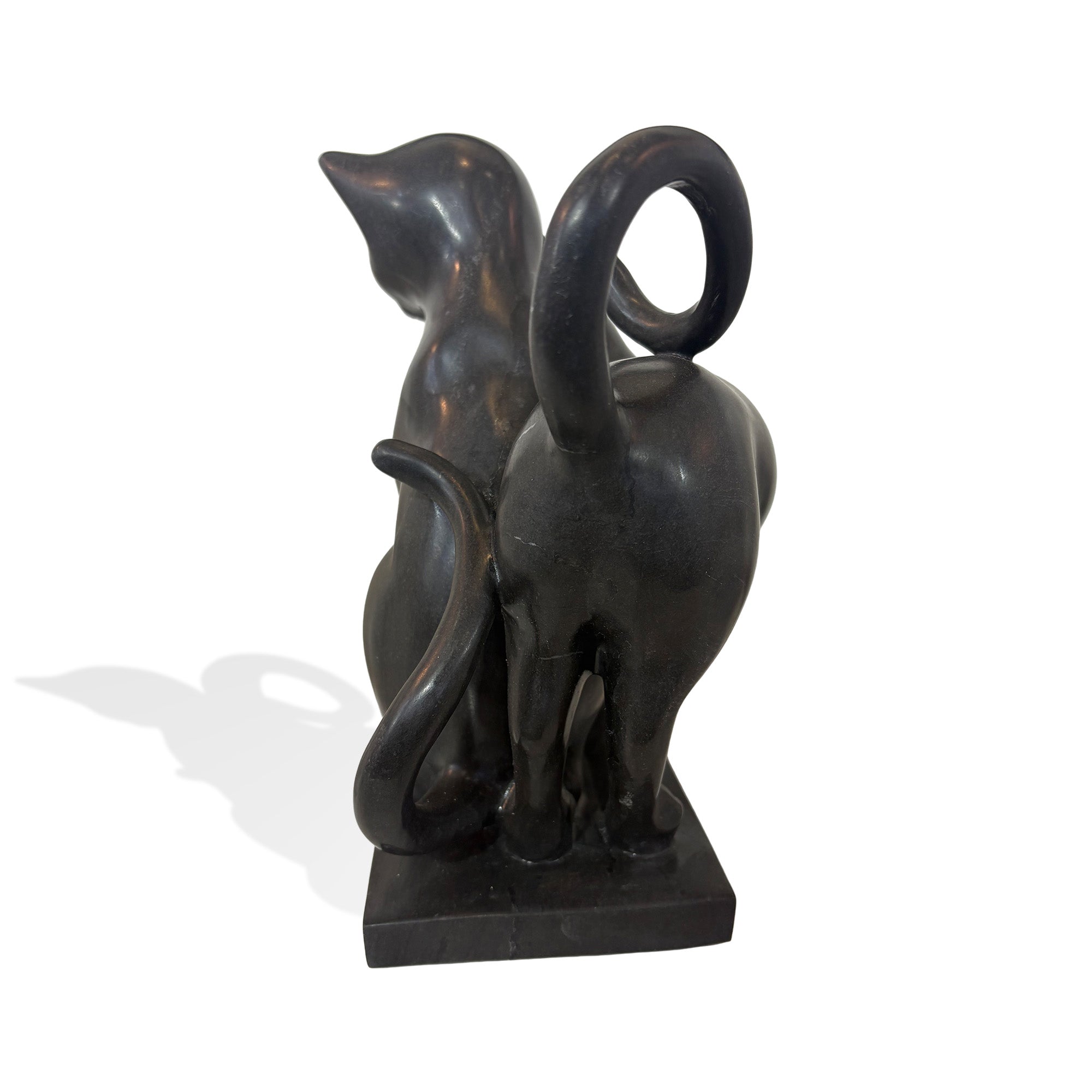 Side back view of black stone cat sculpture showing two cats leaning together with raised curved tails and a polished stone finish
