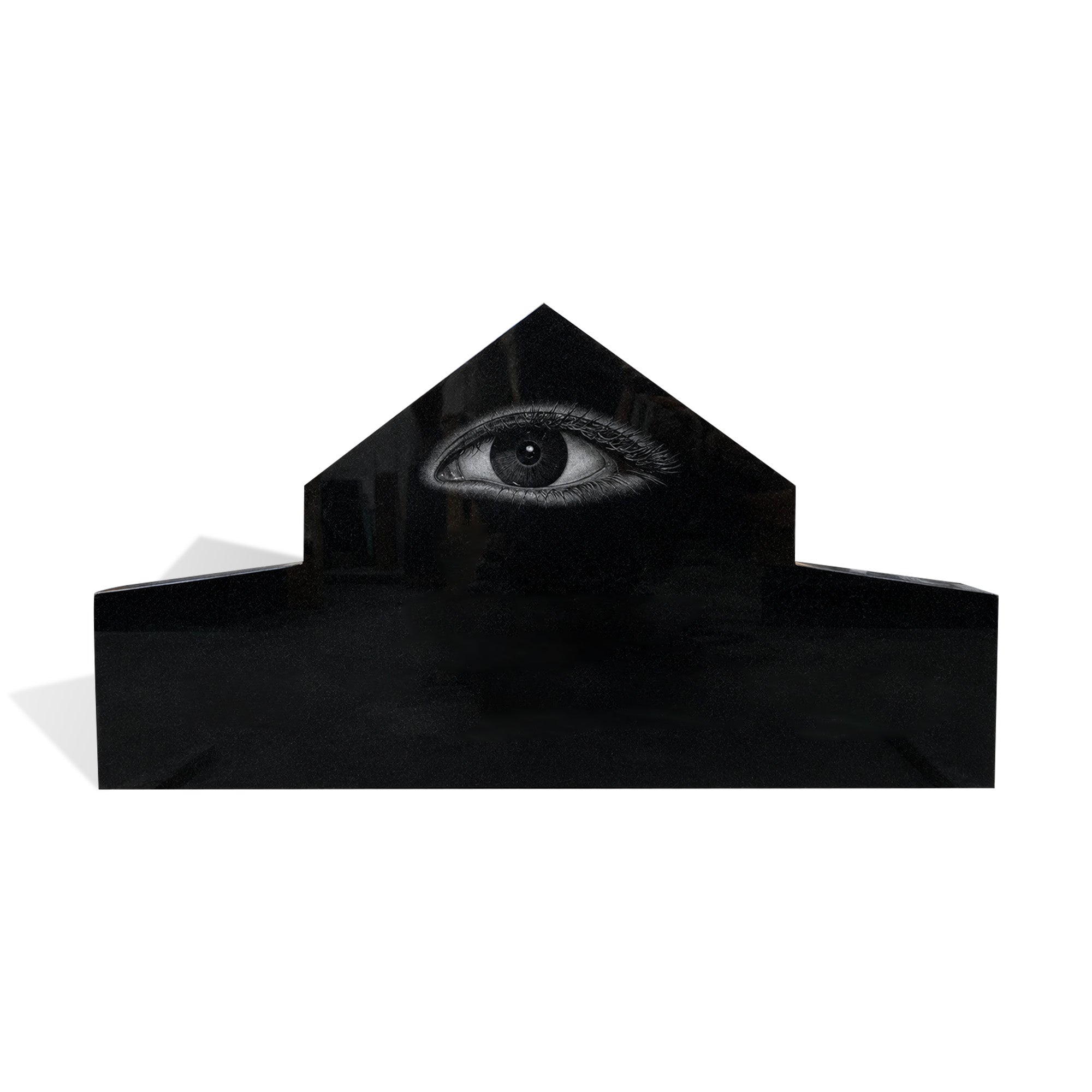 Black granite memorial headstone with polished surface, peaked center top, extended side base, and detailed engraved eye design on white background