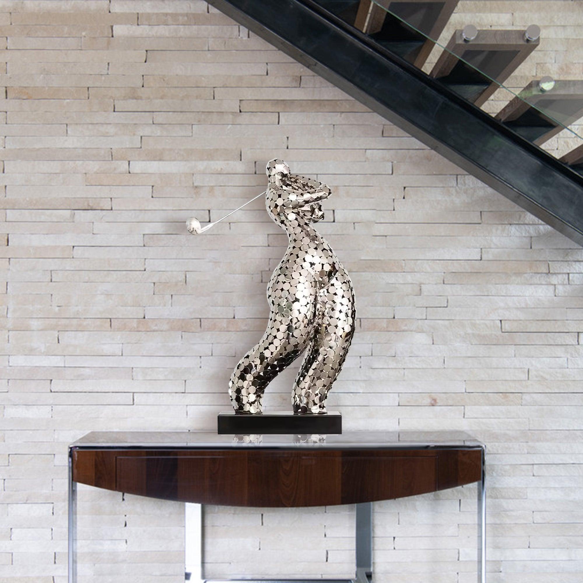 Abstract stainless steel sculpture of a golfer in motion, featuring a mosaic design and placed on a wooden table against a textured wall in a modern indoor setting.