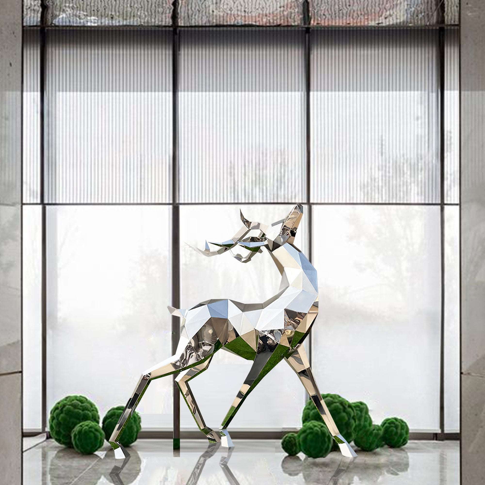 Mirror polished stainless steel elk sculpture with its head held high, reflecting light and surroundings, placed in an elegant indoor setting with large windows.