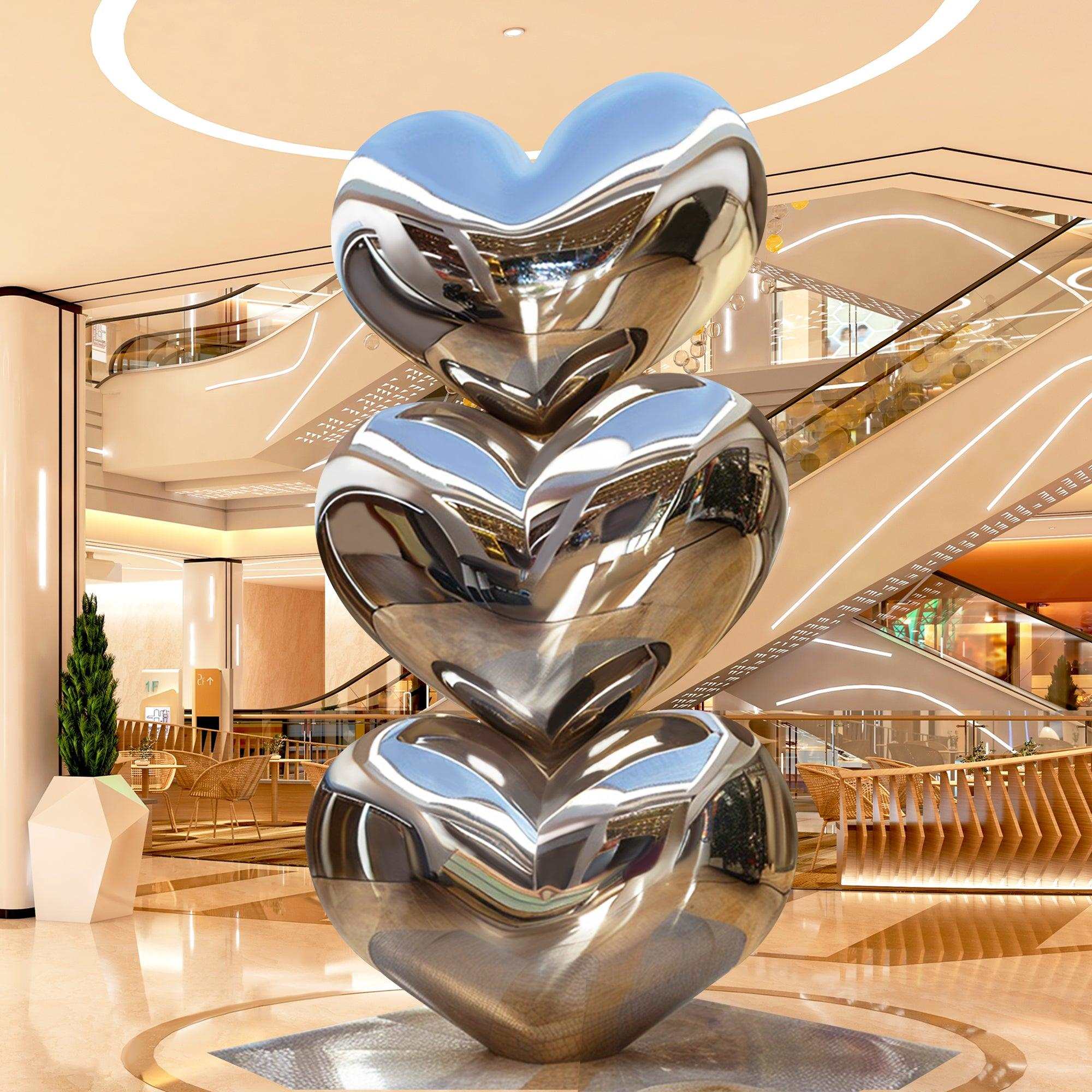 mirror finish three stack heart stainless steel sculpture standing in a mall lobby