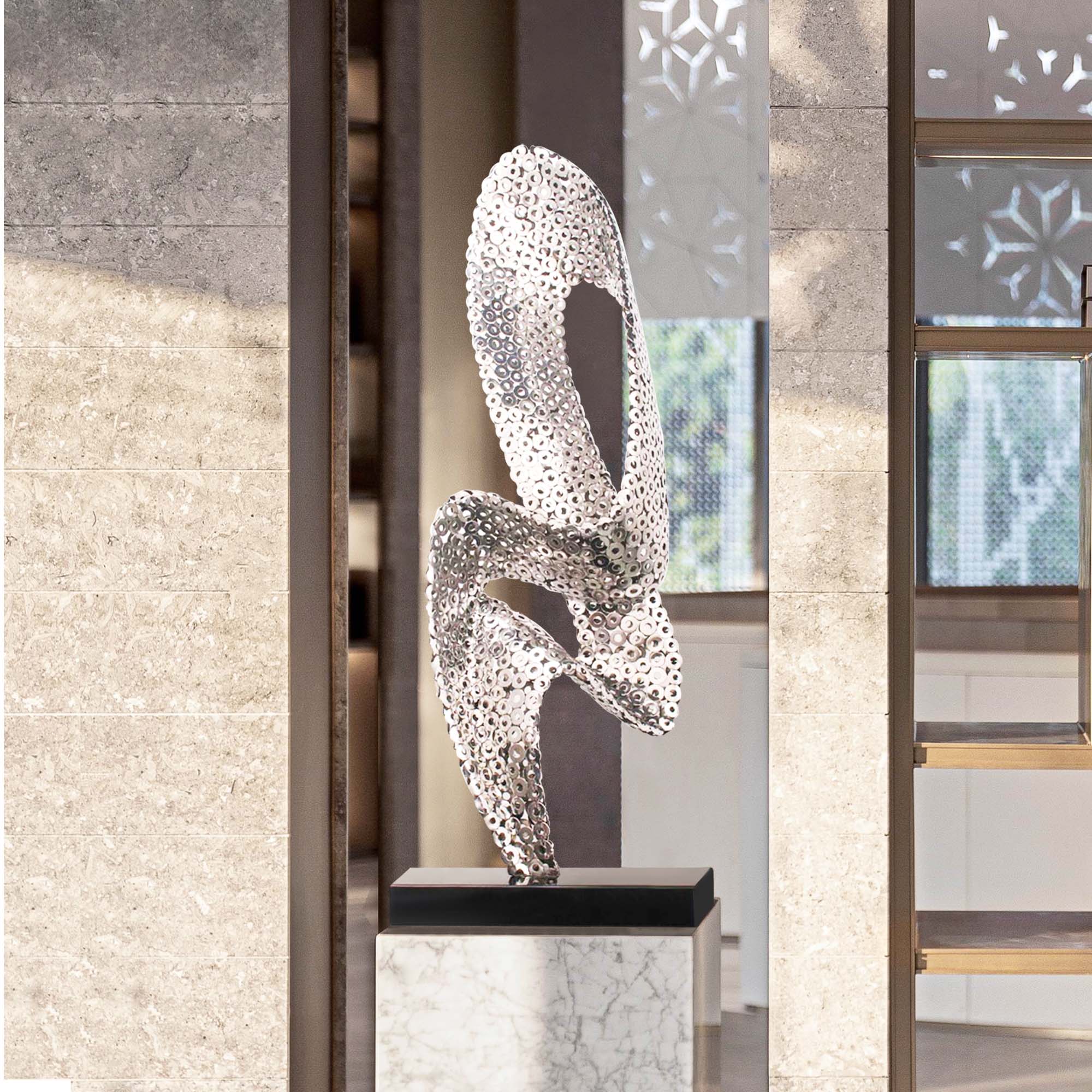 Modern abstract silver sculpture with a perforated metallic design, displayed in a contemporary interior.