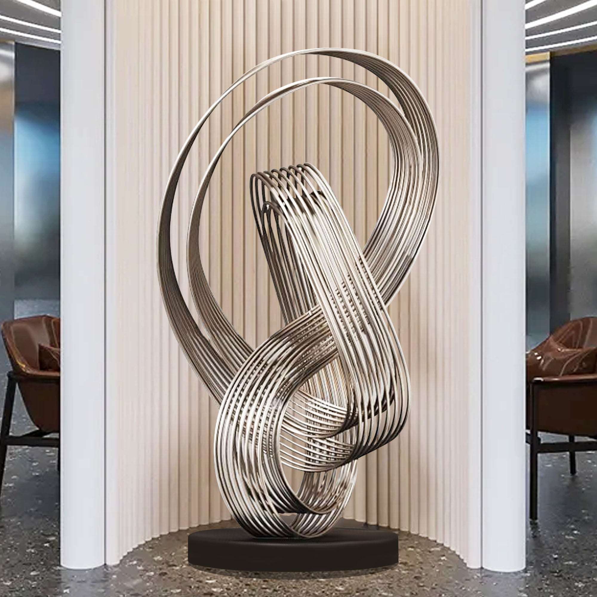 Polished abstract metal floor sculpture with flowing, intertwined lines displayed in a modern indoor setting.